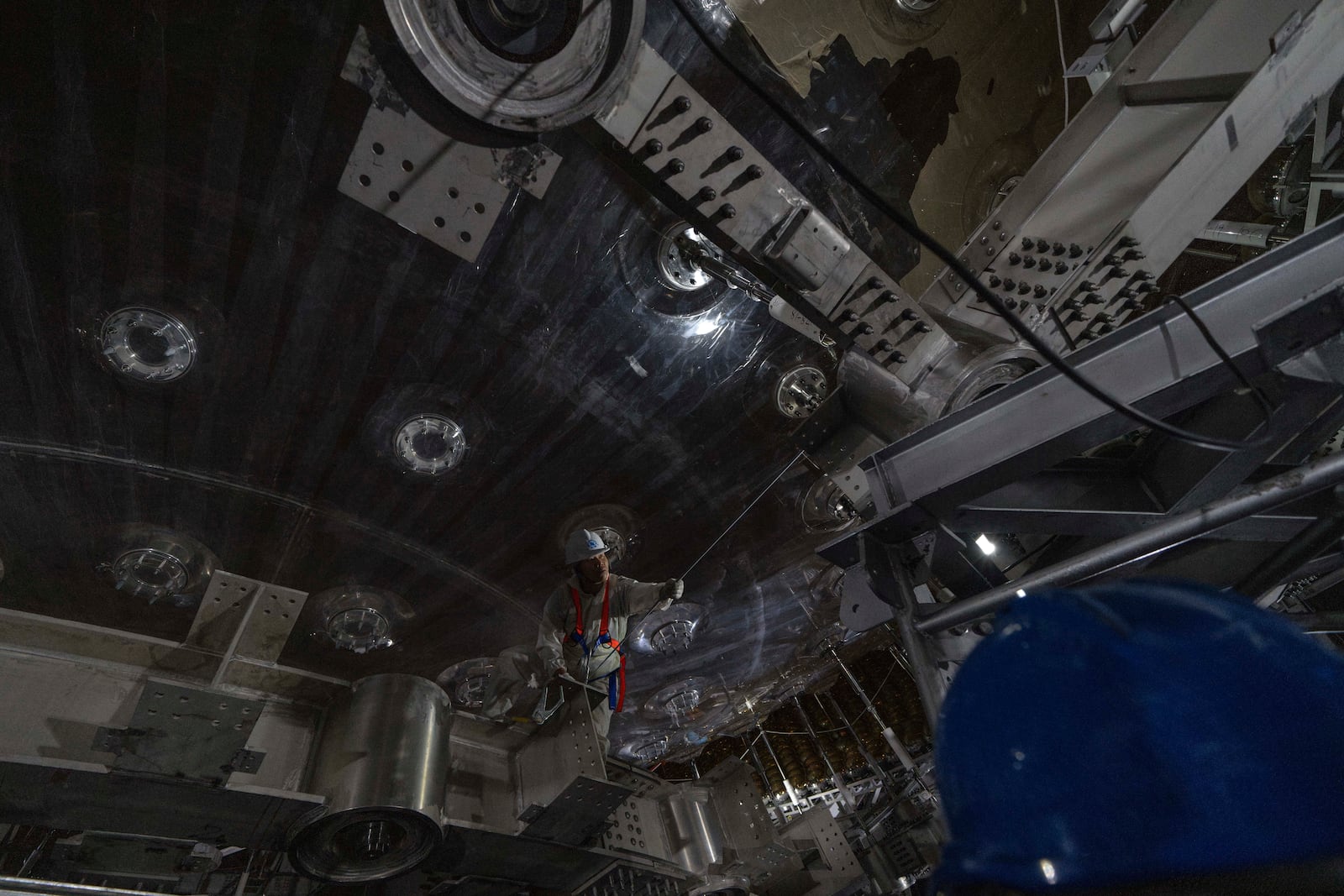 A worker labors on the underside of the cosmic detector located 2297 feet (700 meters) underground at the Jiangmen Underground Neutrino Observatory in Kaiping, southern China's Guangdong province on Friday, Oct. 11, 2024. (AP Photo/Ng Han Guan)