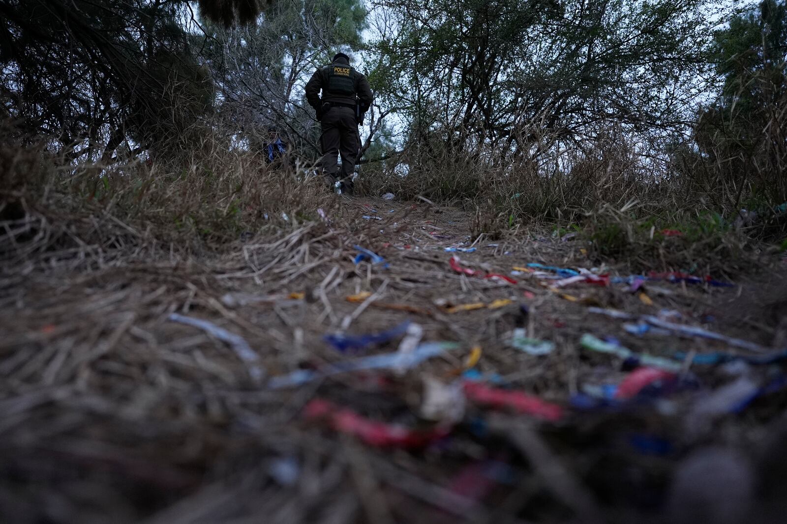 A border patrol agent walks along a trail littered with bracelets used by human smuggling groups near the Rio Grande at the U.S.-Mexico border, Thursday, Feb. 13, 2025, in McAllen, Texas. (AP Photo/Eric Gay)