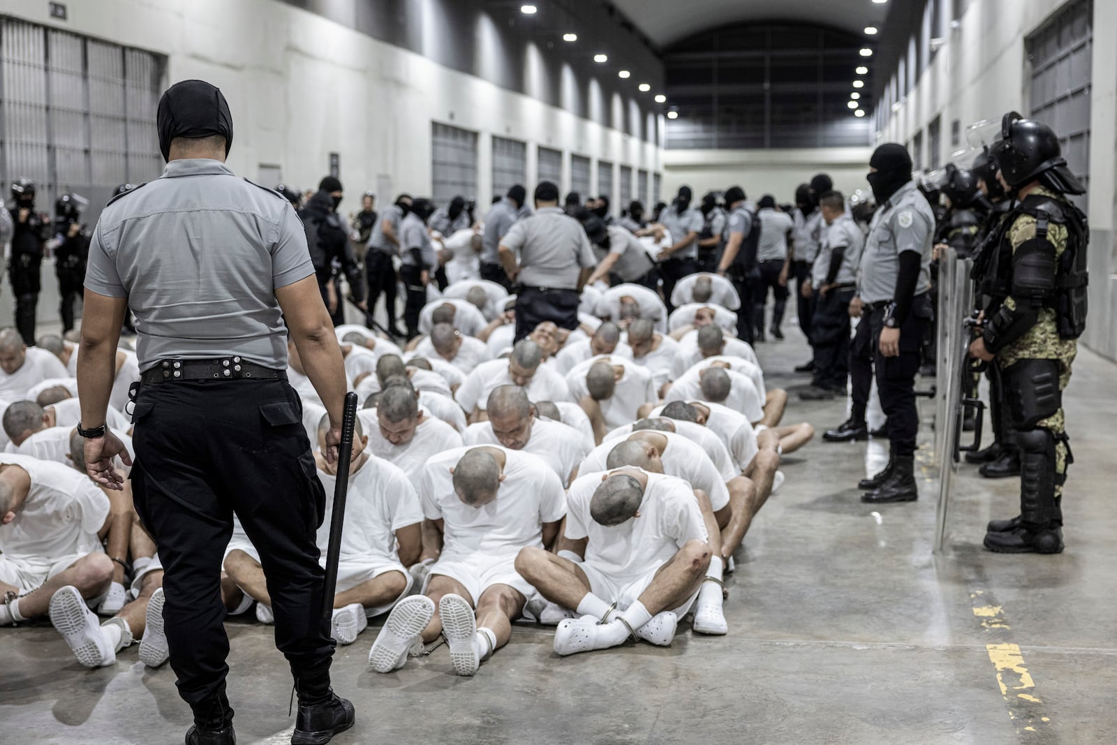 In this photo provided by El Salvador's presidential press guards, a prison guard transfers deportees from the U.S., alleged to be Venezuelan gang members, to the Terrorism Confinement Center in Tecoluca, El Salvador, Sunday, March 16, 2025. (El Salvador presidential press office via AP)