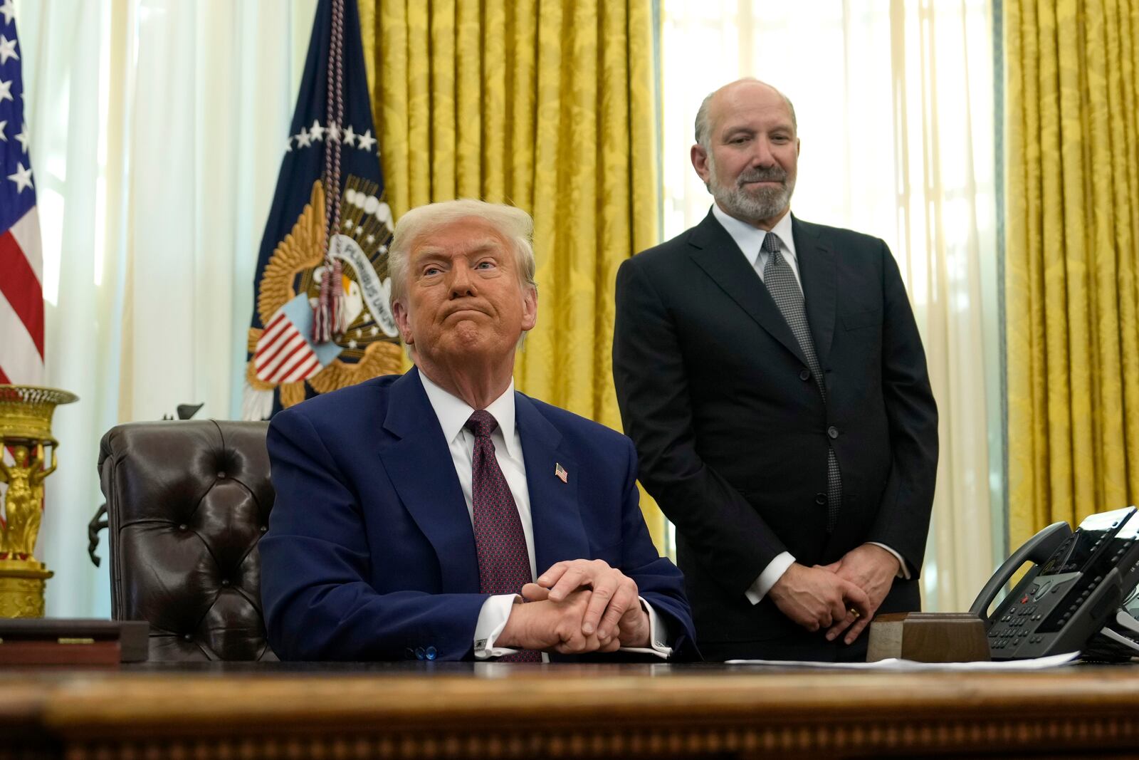 President Donald Trump listens to a question from a reporter as Commerce Secretary nominee Howard Lutnick watches after Trump signed an executive order in the Oval Office of the White House, Thursday, Feb. 13, 2025, in Washington. (AP Photo/Ben Curtis)