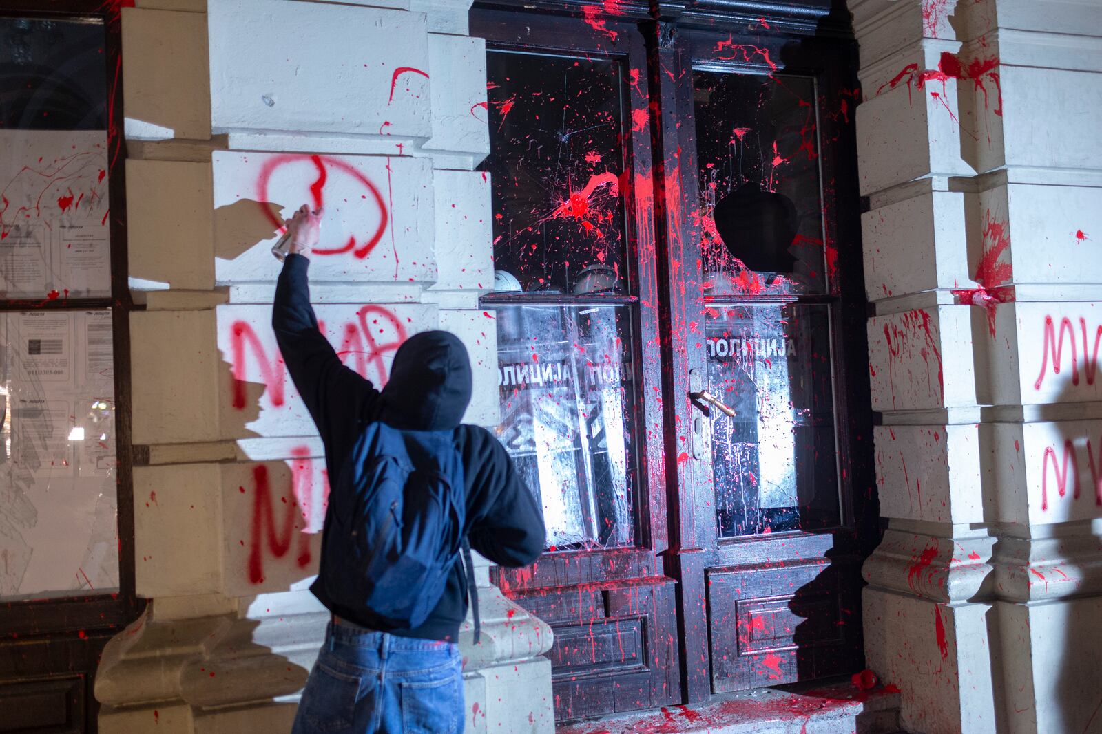 A protester paints grafitti on the City Hall building during a protest in rage over last week's collapse of a concrete canopy at the railway station that killed 14 people, in Novi Sad, Serbia, Tuesday, Nov. 5, 2024. (AP Photo/Marko Drobnjakovic)