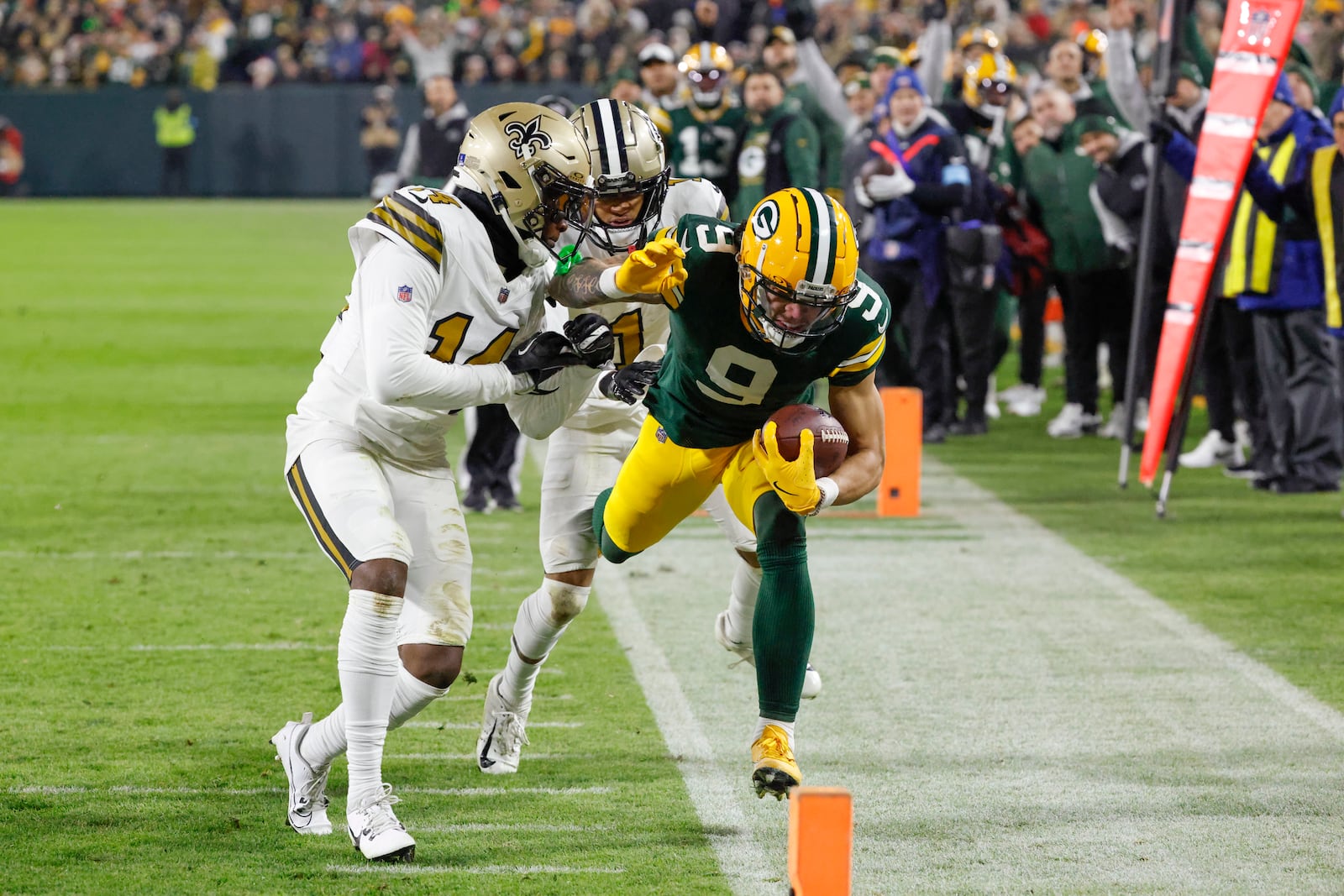 Green Bay Packers wide receiver Christian Watson (9) carries against New Orleans Saints cornerback Alontae Taylor (1) and cornerback Kool-Aid McKinstry (14) during the first half of an NFL football game, Monday, Dec. 23, 2024, in Green Bay, Wis. (AP Photo/Mike Roemer)