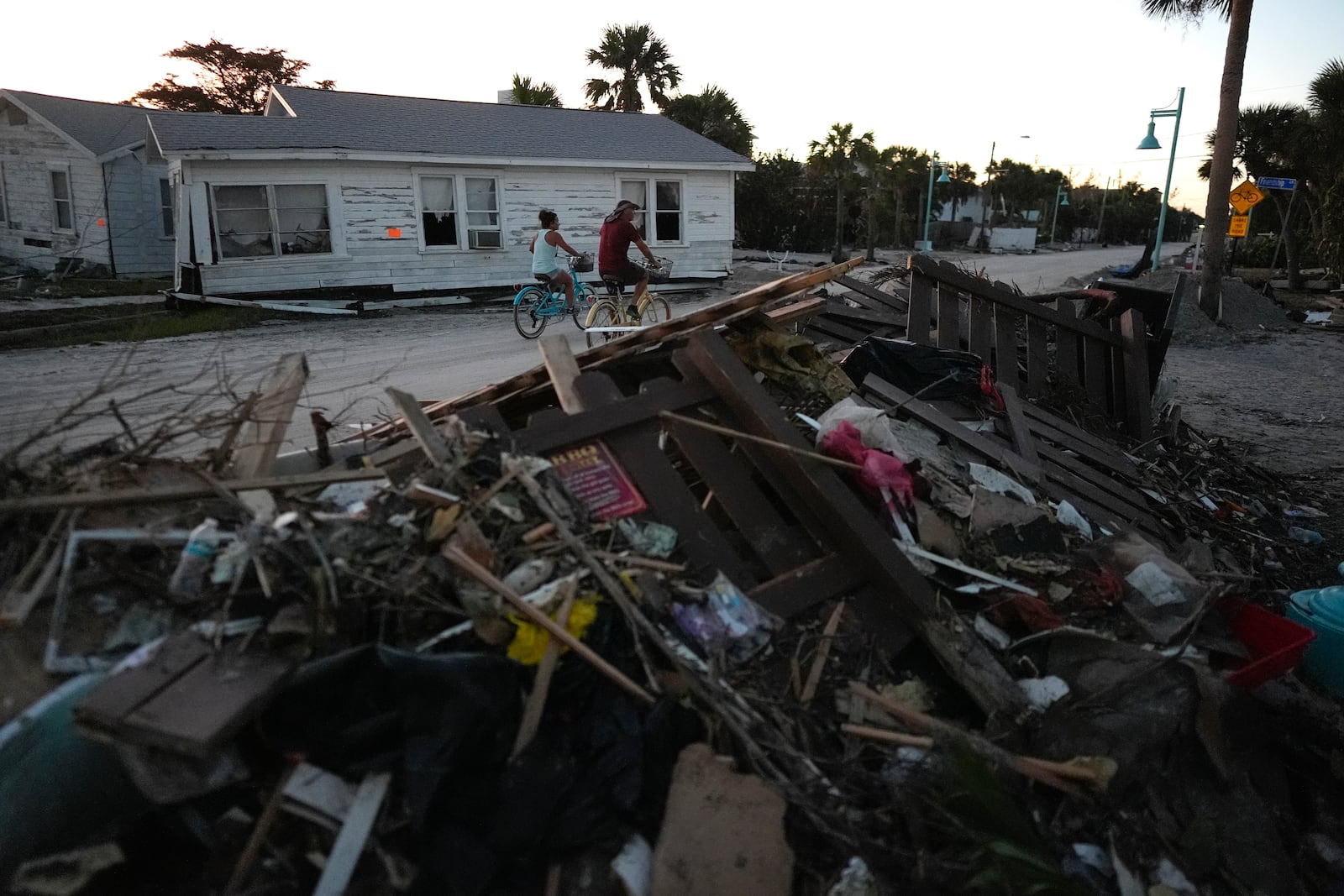 FILE - People bike past damaged homes and debris left by Hurricane Milton, on the sand-coated main road of southern Manasota Key, already cleared of feet of sand, in Englewood, Fla., Oct. 13, 2024. (AP Photo/Rebecca Blackwell, File)