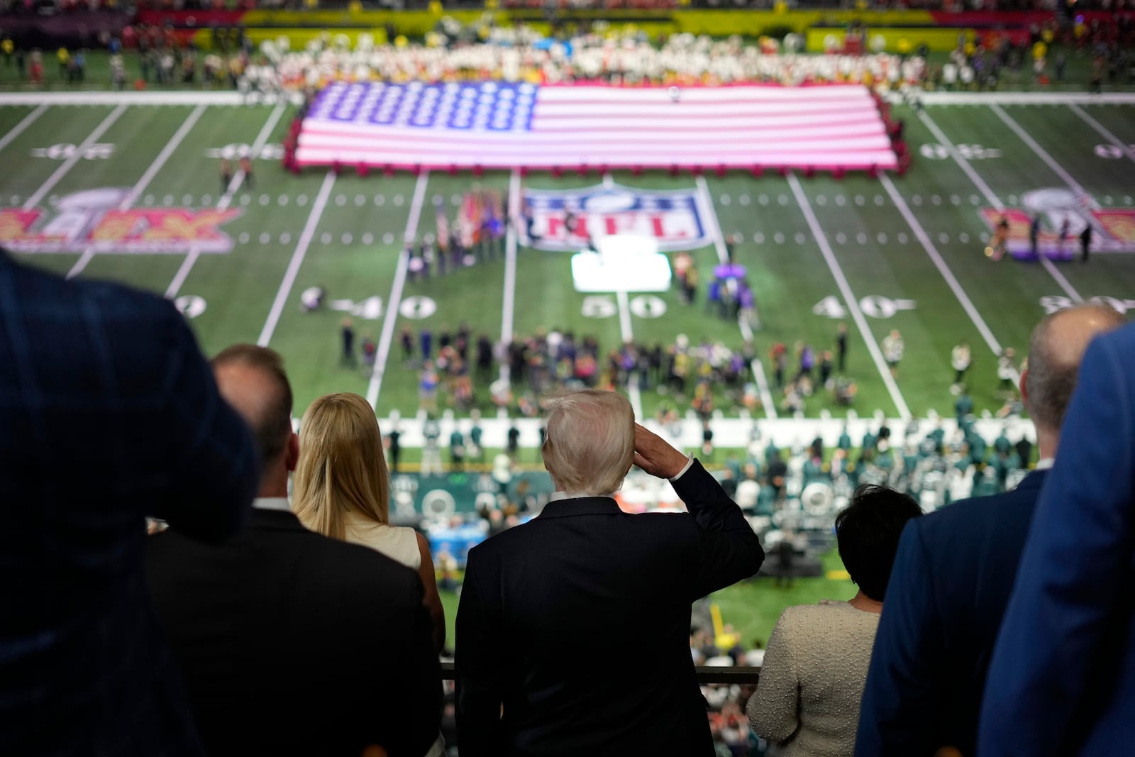 President Donald Trump, center, salutes as Jon Batiste performs the national anthem at the NFL Super Bowl 59 football game between the Philadelphia Eagles and the Kansas City Chiefs, Sunday, Feb. 9, 2025, in New Orleans. (AP Photo/Ben Curtis)