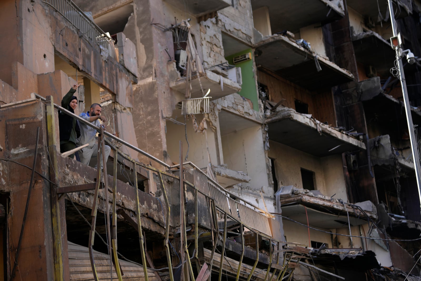 Residents stand on their apartment balcony at a building that was destroyed by an Israeli airstrike in Dahiyeh, in the southern suburb of Beirut, Lebanon, Monday, Nov. 11, 2024. (AP Photo/Hussein Malla)