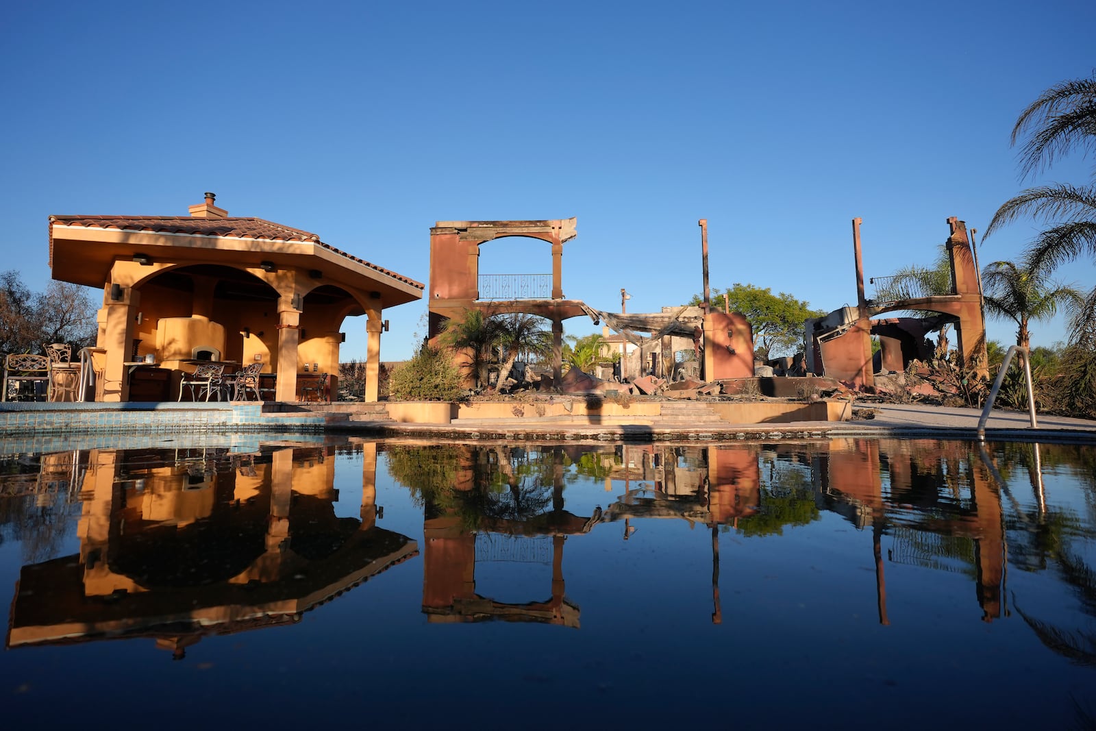 A home destroyed by the Mountain Fire is reflected in water from a swimming pool in Camarillo, Calif., Friday, Nov. 8, 2024. (AP Photo/Jae C. Hong)