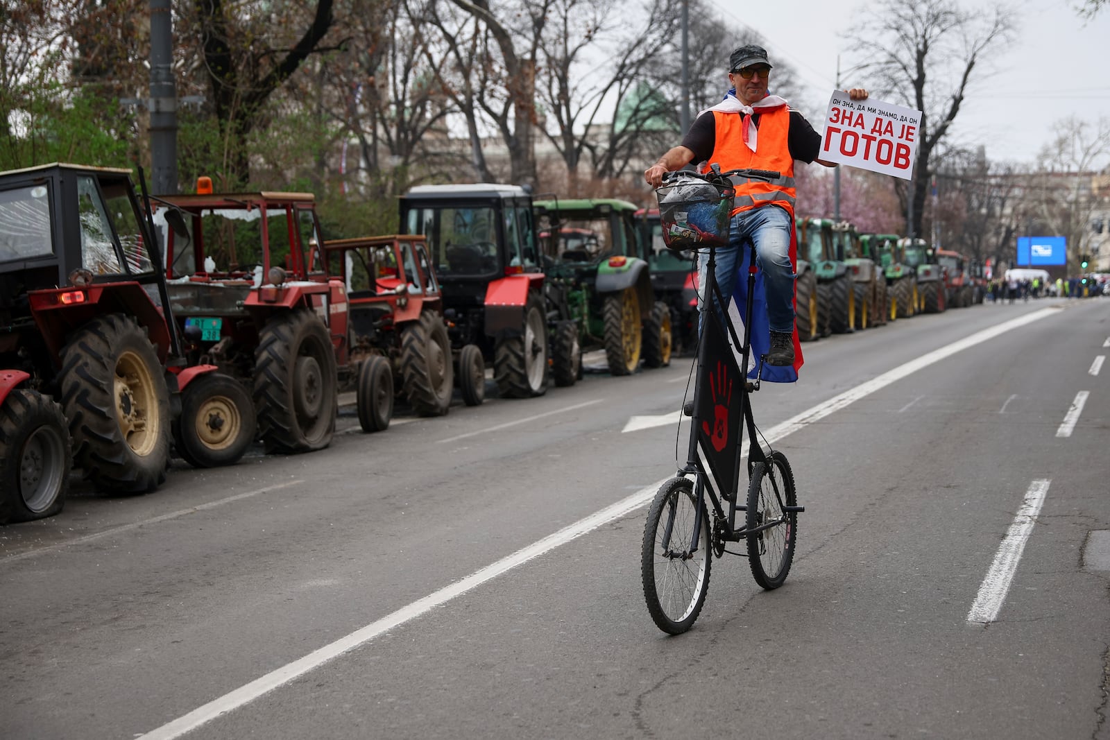 A protester riding past parked tractors carries a placard reading 'he knows he is done' during a major rally against populist President Aleksandar Vucic and his government, in downtown Belgrade, Serbia, Saturday, March 15, 2025. (AP Photo/Armin Durgut)