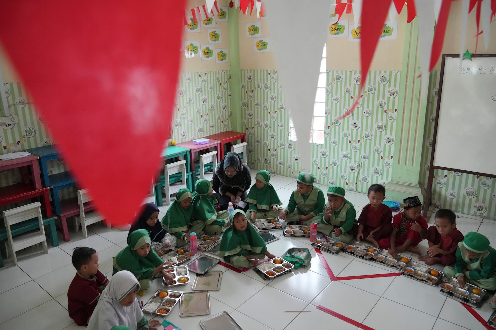 Students sit on the floor as they have their meals during the kick off of President Prabowo Subianto's ambitious free meal program to feed children and pregnant women nationwide despite critics saying that its required logistics could hurt Indonesia's state finances and economy at Early Childhood Education and Development in Jakarta, Indonesia, Monday, Jan. 6, 2025. (AP Photo/Achmad Ibrahim)