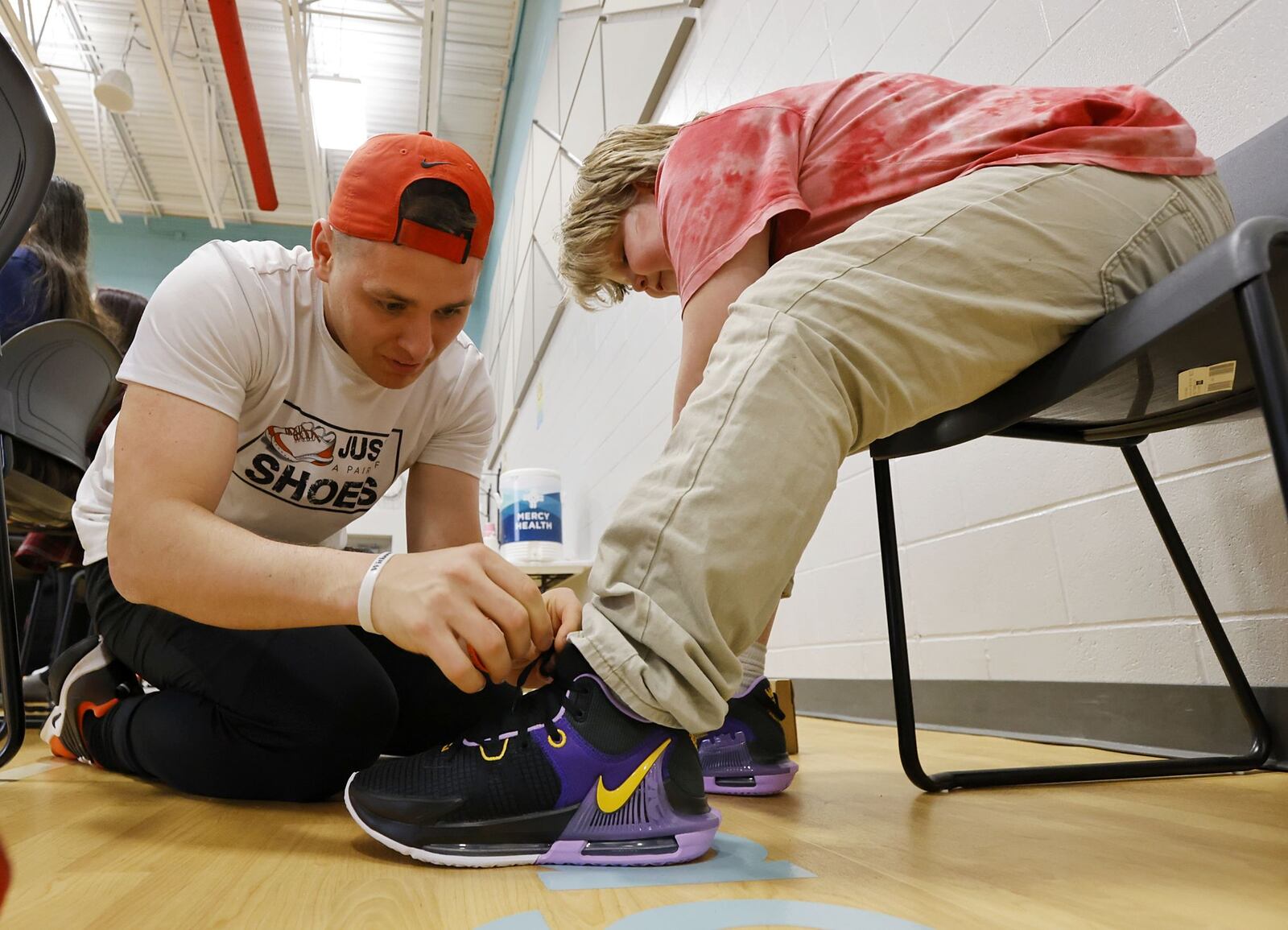 Liam Crosswell gets help trying on shoes from Matt Cline, founder of non-profit Just a Pair of Shoes. Fifth-grade students at Fairfield Central Elementary were given new shoes during a surprise assembly Friday, March 15, 2024 thanks to some fundraising and help from an Ohio-based, non-profit organization called Just a Pair of Shoes. The organization is focused on one mission: to put quality name-brand shoes on young students' feet, boost confidence, and create a sense of belonging. Each fifth grader will be outfitted with a pair of Nike shoes. They got the sizes by having the students measure their feet under the guise of a math lesson. NICK GRAHAM/STAFF