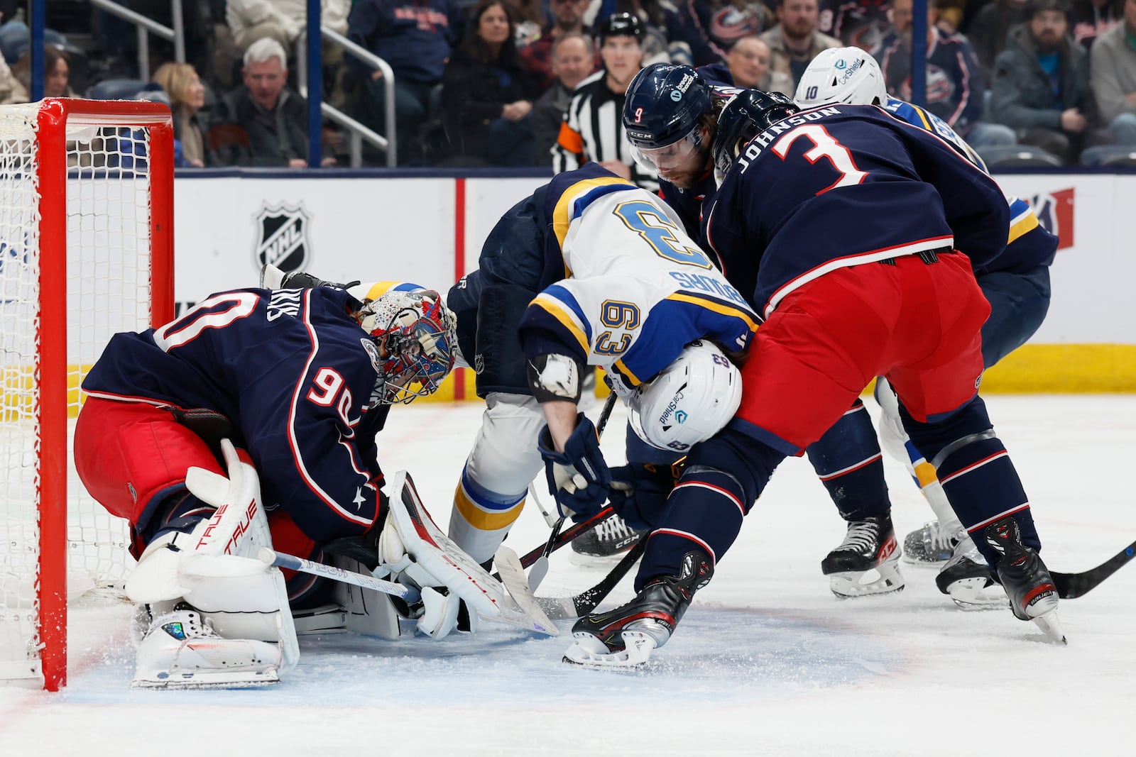 Columbus Blue Jackets' Elvis Merzlikins, left, makes a save as teammate Jack Johnson, right, and St. Louis Blues' Jake Neighbours collide in front of the net during the first period of an NHL hockey game Saturday, Jan. 4, 2025, in Columbus, Ohio. (AP Photo/Jay LaPrete)