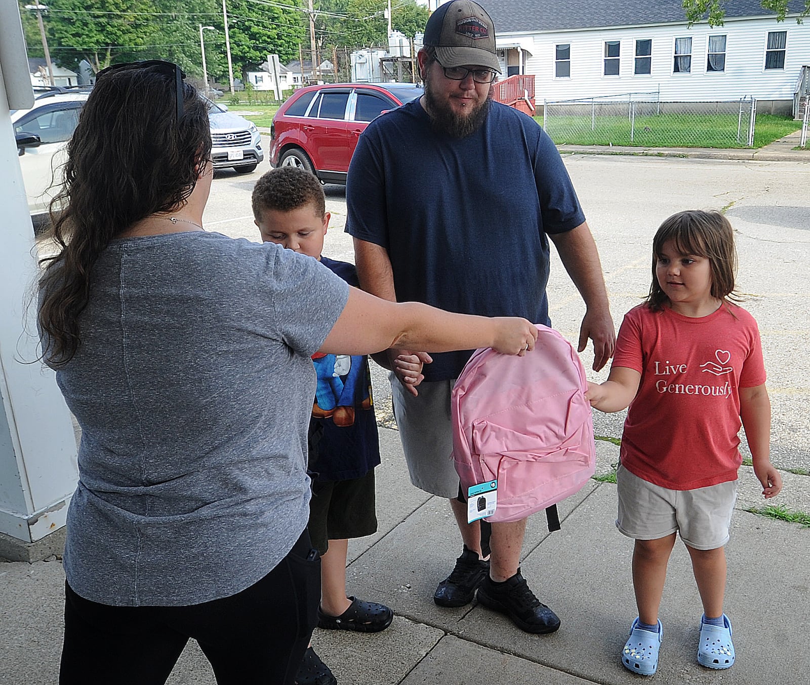 Jessica Provost, a 6th grade teacher in the Mad River School  District hands free backpacks to Kenny ,age 8 and his sister, Adalyn Hoskins, age 6, with their father, Kenneth at the Overlook Community Center Friday, Aug. 25, 2023. MARSHALL GORBY\STAFF