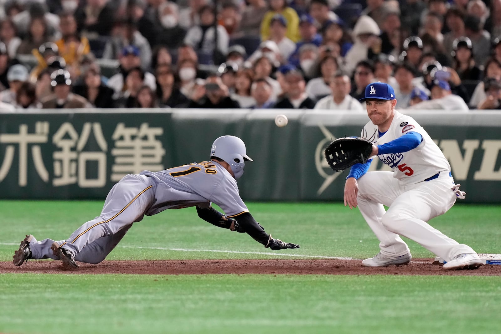 Hanshin Tigers' Takumu Nakano, left, slides into first base next to Los Angeles Dodgers' Freddie Freeman during the fifth inning in an MLB Japan Series exhibition baseball game, Sunday, March 16, 2025, in Tokyo. (AP Photo/Eugene Hoshiko)