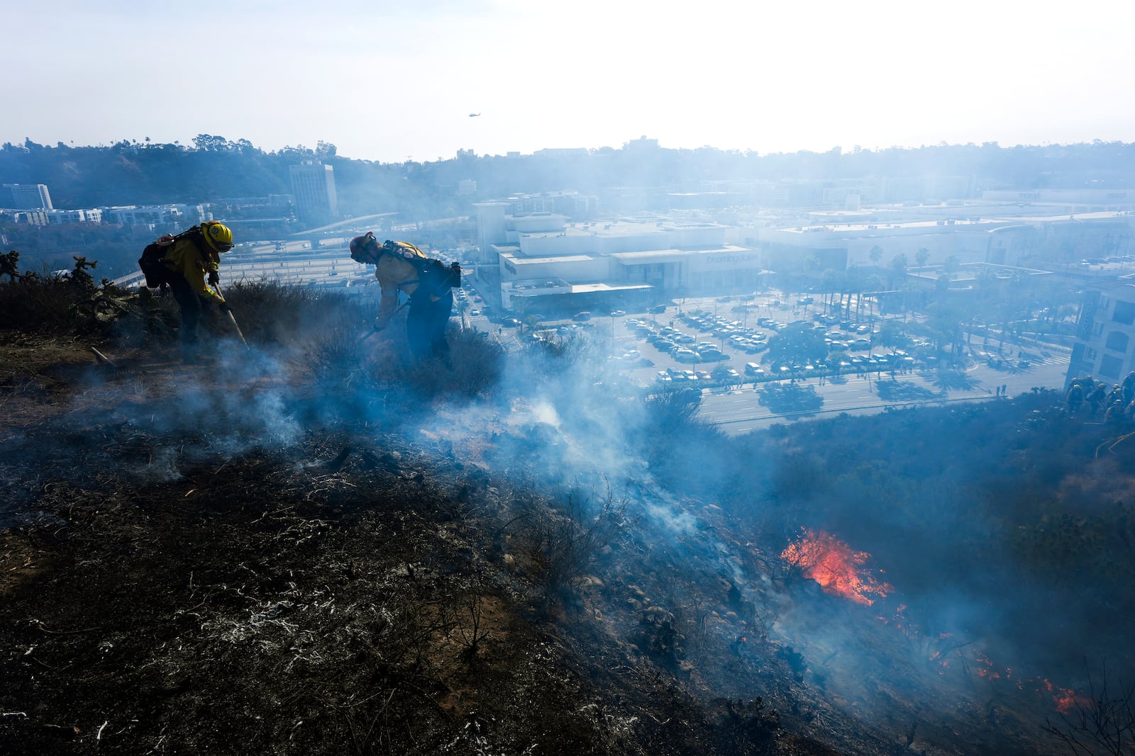 San Diego firefighters knock down a small brush along a hillside over the Mission Valley Shopping Mall in San Diego on Tuesday, Jan. 21, 2025. (AP Photo/Gregory Bull)