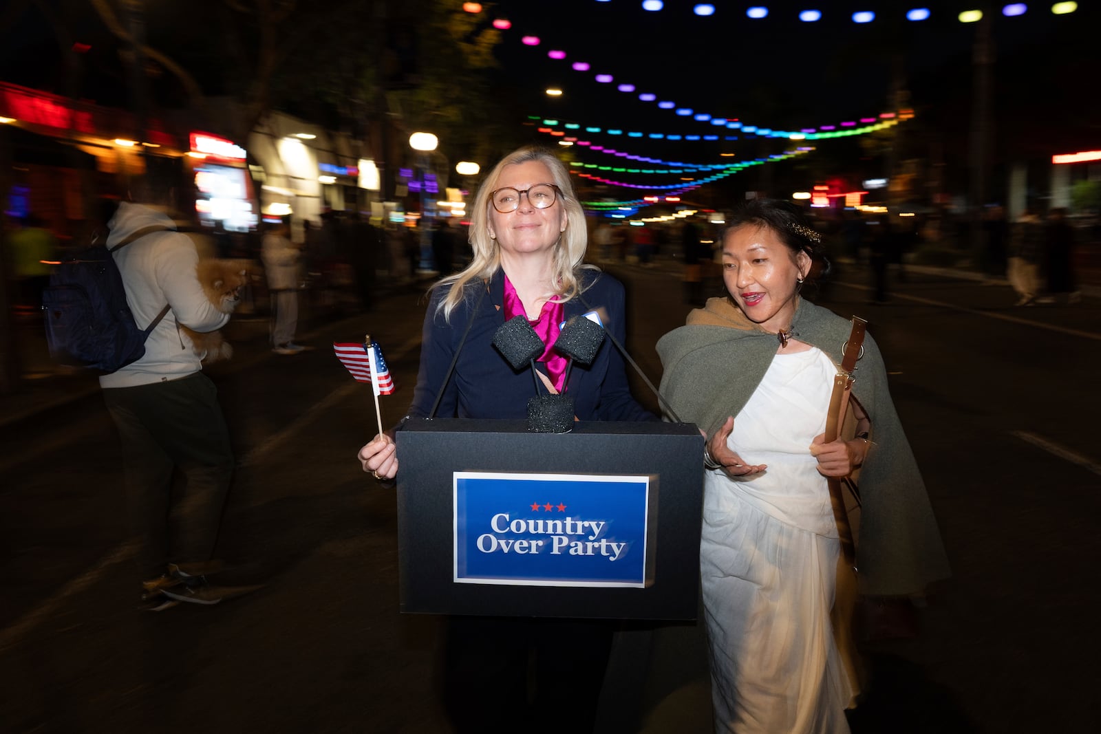 Dressed as Liz Cheney, Maggie Langrick, left, walks with Lulu Hansen during the Halloween Carnival in West Hollywood, Calif., Thursday, Oct. 31, 2024. (AP Photo/Jae C. Hong)