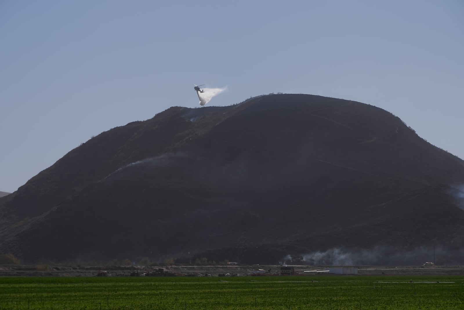 A helicopter drops water on flames Thursday, Jan. 23, 2025 in Camarillo, Calif,, where the Laguna Fire fire broke out. (AP Photo/Brittany Peterson)