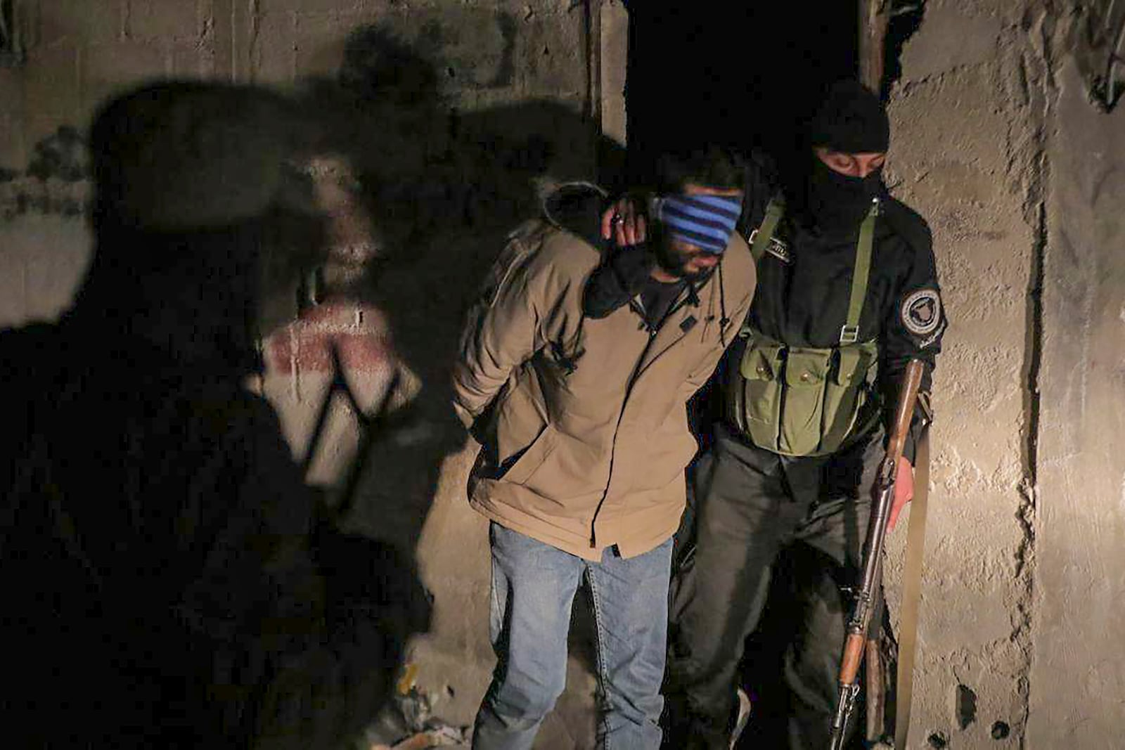 In this photo released by Syrian State TV, one of four suspects arrested in connection with an alleged plot by ISIS is escorted by security officers in Damascus, Syria, Saturday, Jan. 11, 2025. Syrian intelligence officials, operating under the country's new de facto government, thwarted an attempt by ISIS to detonate a bomb at the Shiite shrine of Sayyida Zaynab in the Damascus suburb, according to state media reports on Saturday.(Syrian State TV via AP)