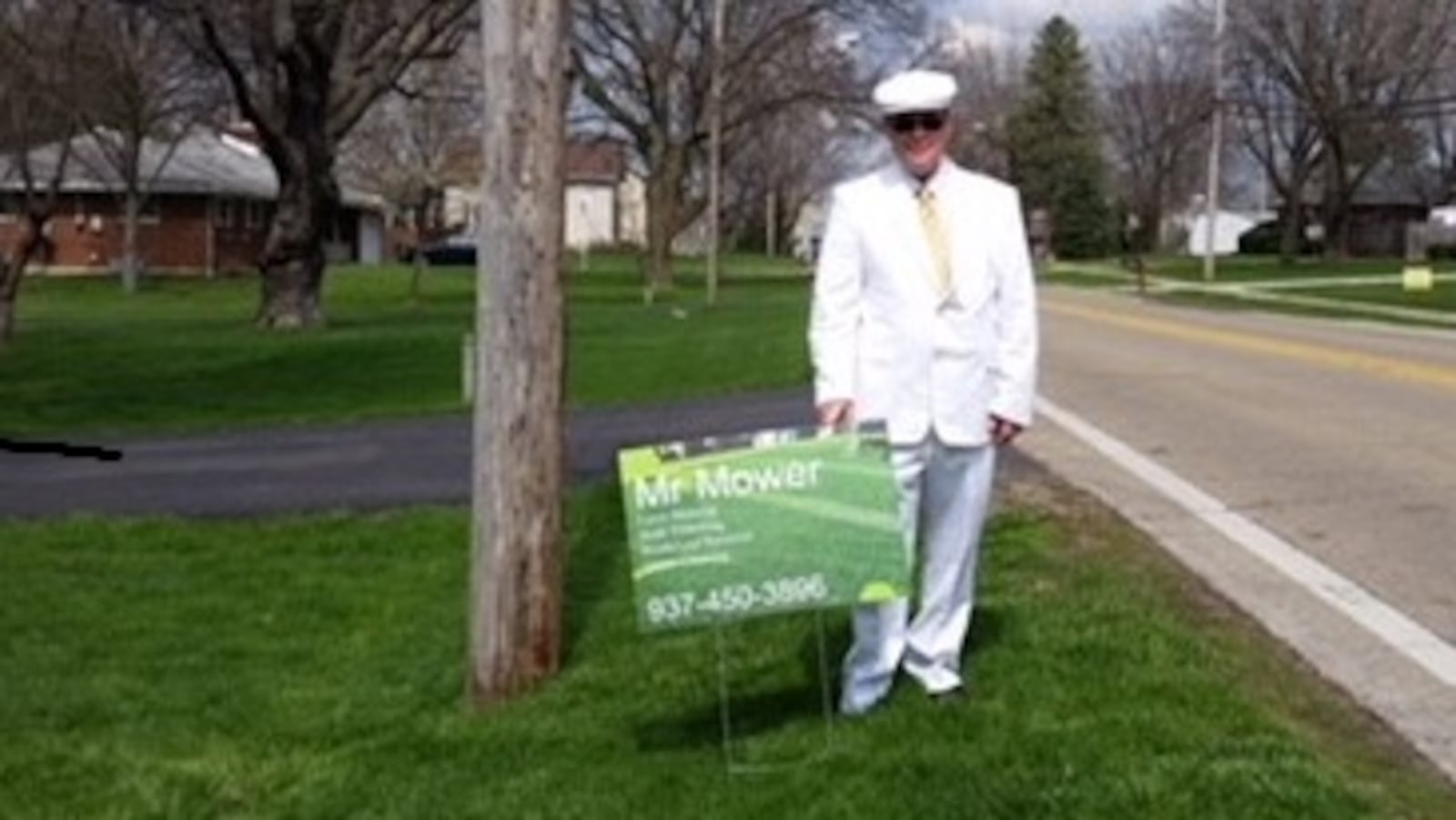 Joshua Vanderpool stands behind a sign for his lawn mowing business