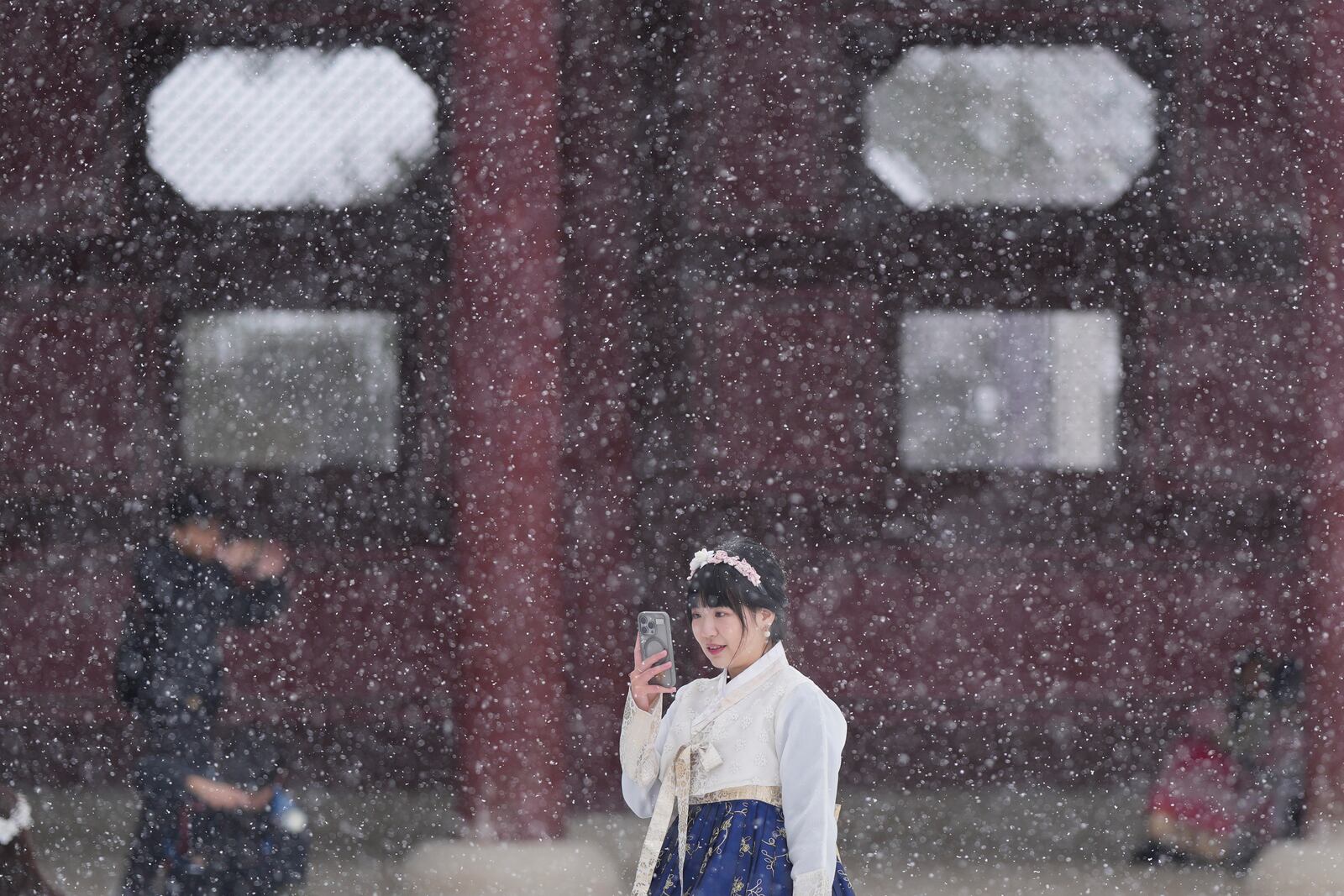 Chan Yian from Taiwan holds her smartphone in snow at the Gyeongbok Palace, one of South Korea's well-known landmarks, in Seoul, South Korea, Wednesday, Nov. 27, 2024. (AP Photo/Lee Jin-man)