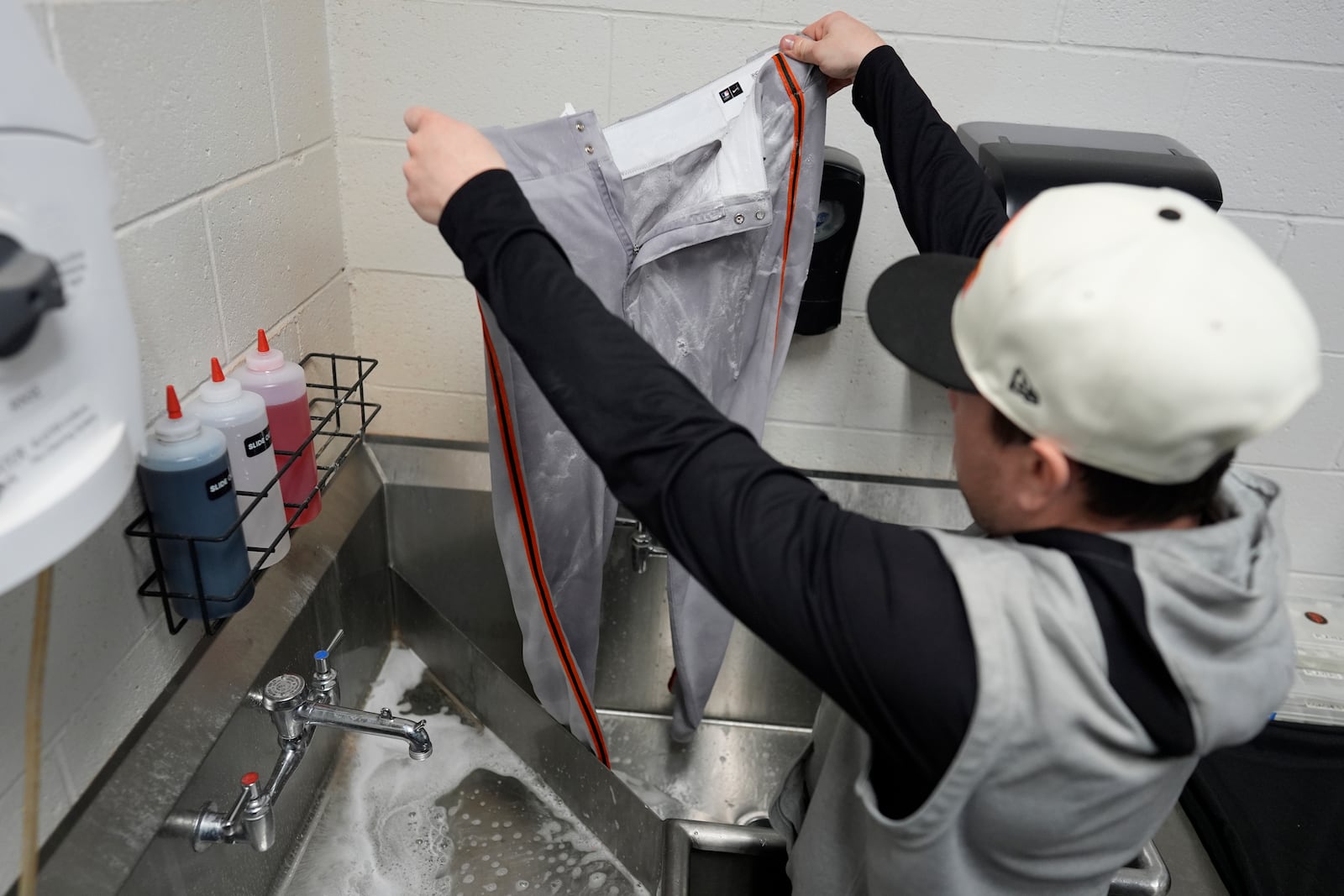 San Francisco Giants clubhouse attendant Riley Halpin removes stains from baseball pants in the laundry room sink during baseball spring training at the team's facility, Monday, Feb. 17, 2025, in Scottsdale, Ariz. (AP Photo/Carolyn Kaster)