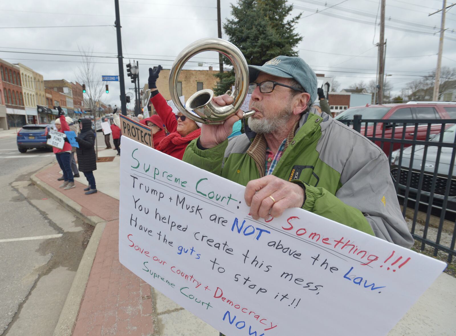 Bob Blazo blows a horn as he joins dozens of people gathered in downtown Niles, Mich., Thursday, March 20, 2025, to protest recent government cuts in the Department of Education. (Don Campbell/The Herald-Palladium via AP)