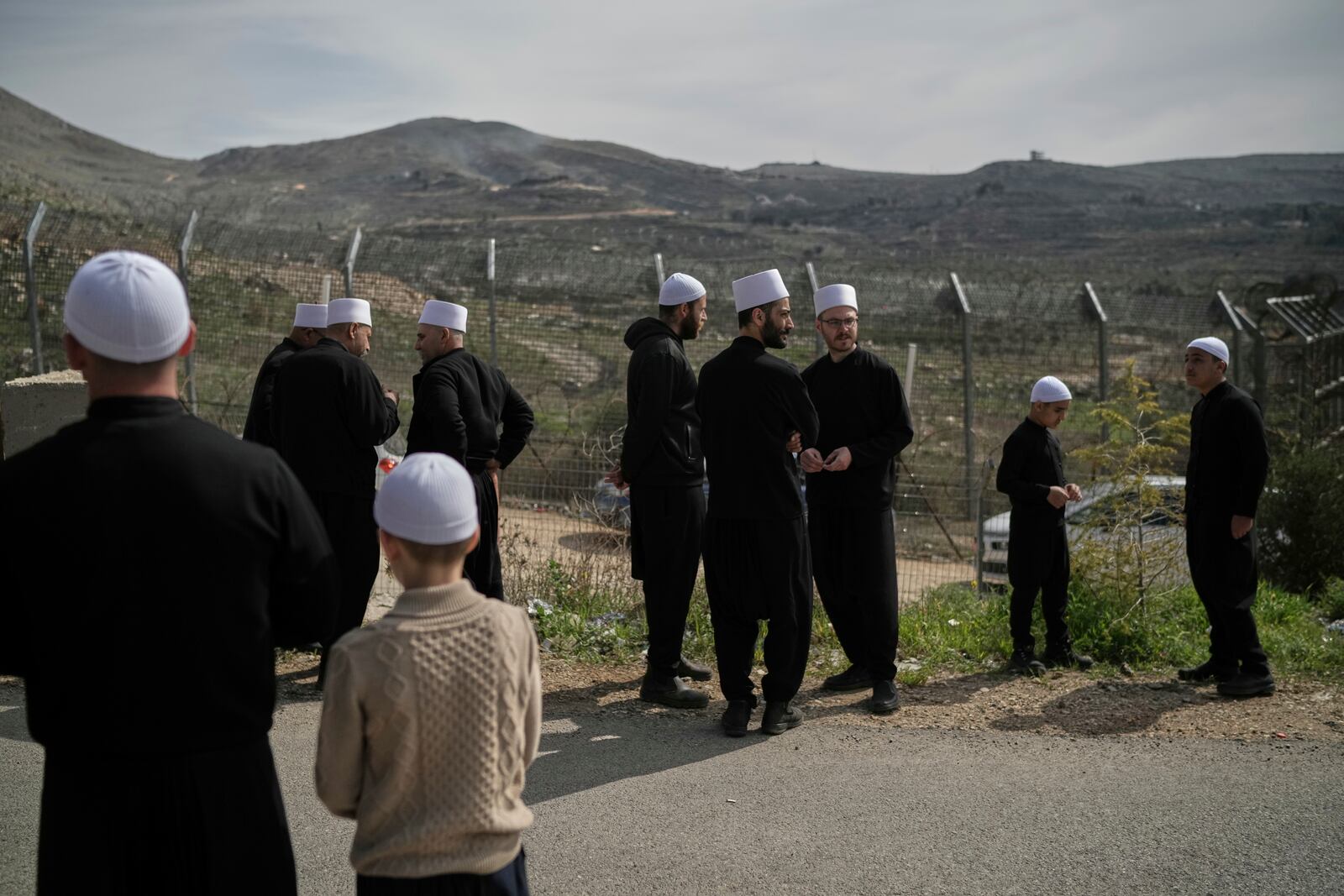 Druze men and boys stand near the border, as they wait for buses carrying members of the Syrian Druze community to cross from Syria in the village of Majdal Shams, located in the Israeli-controlled Golan Heights, Friday, March 14, 2025. (AP Photo/Leo Correa)