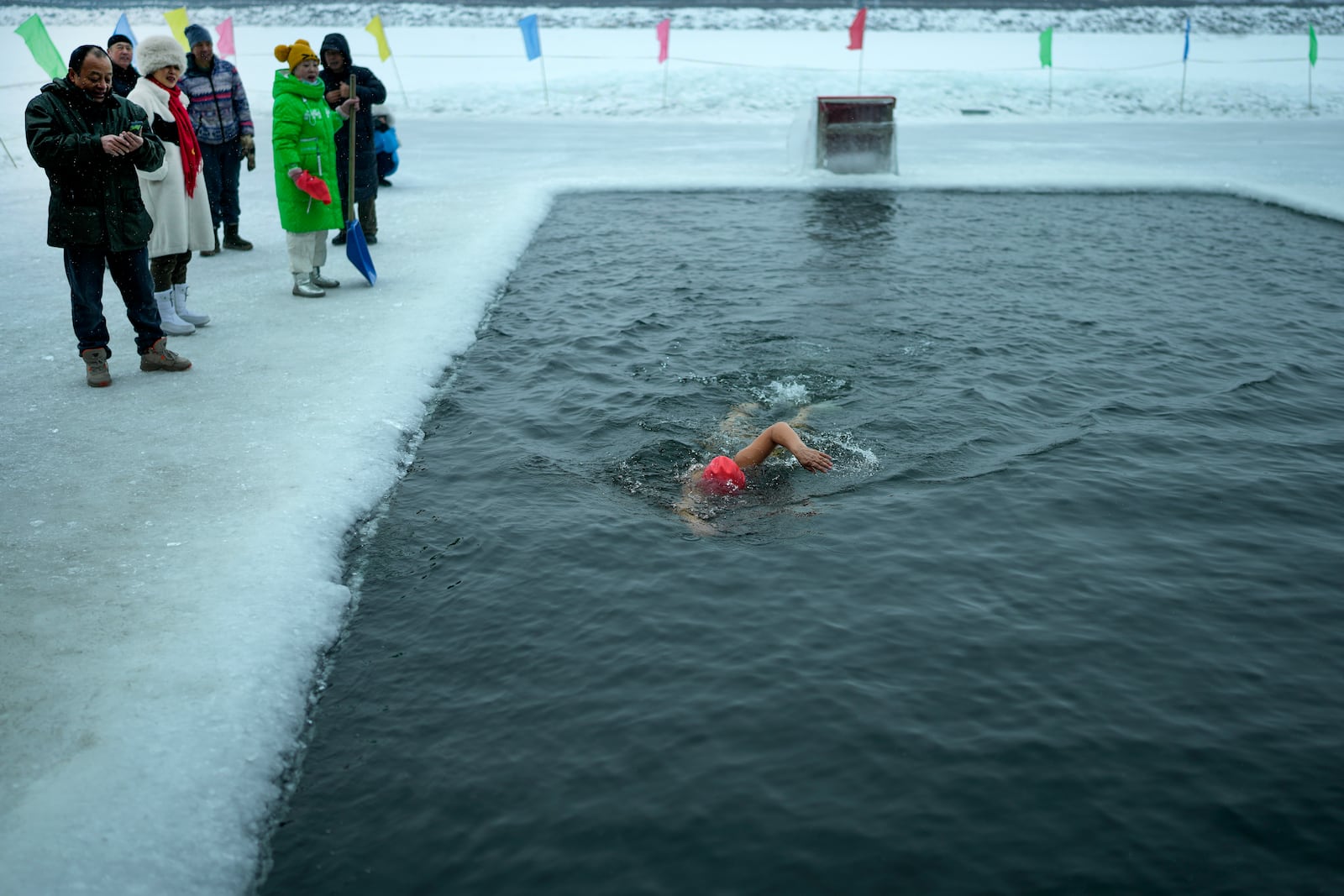 Residents watch a woman swim in a pool carved from ice on the frozen Songhua river in Harbin in northeastern China's Heilongjiang province, Tuesday, Jan. 7, 2025. (AP Photo/Andy Wong)