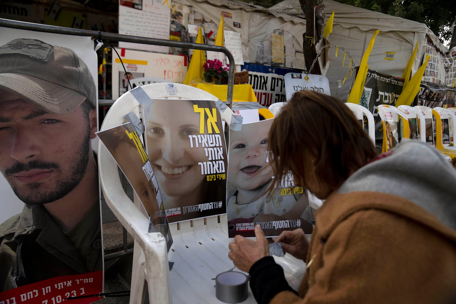 A volunteer tapes posters of Shiri Bibas, center, and her sons Ariel, left, and Kfir, right, who were taken hostage by Hamas militants on Oct. 7, 2023, are displayed on an empty chair in Jerusalem, Wednesday, Feb. 19, 2025. (AP Photo/Maya Alleruzzo)