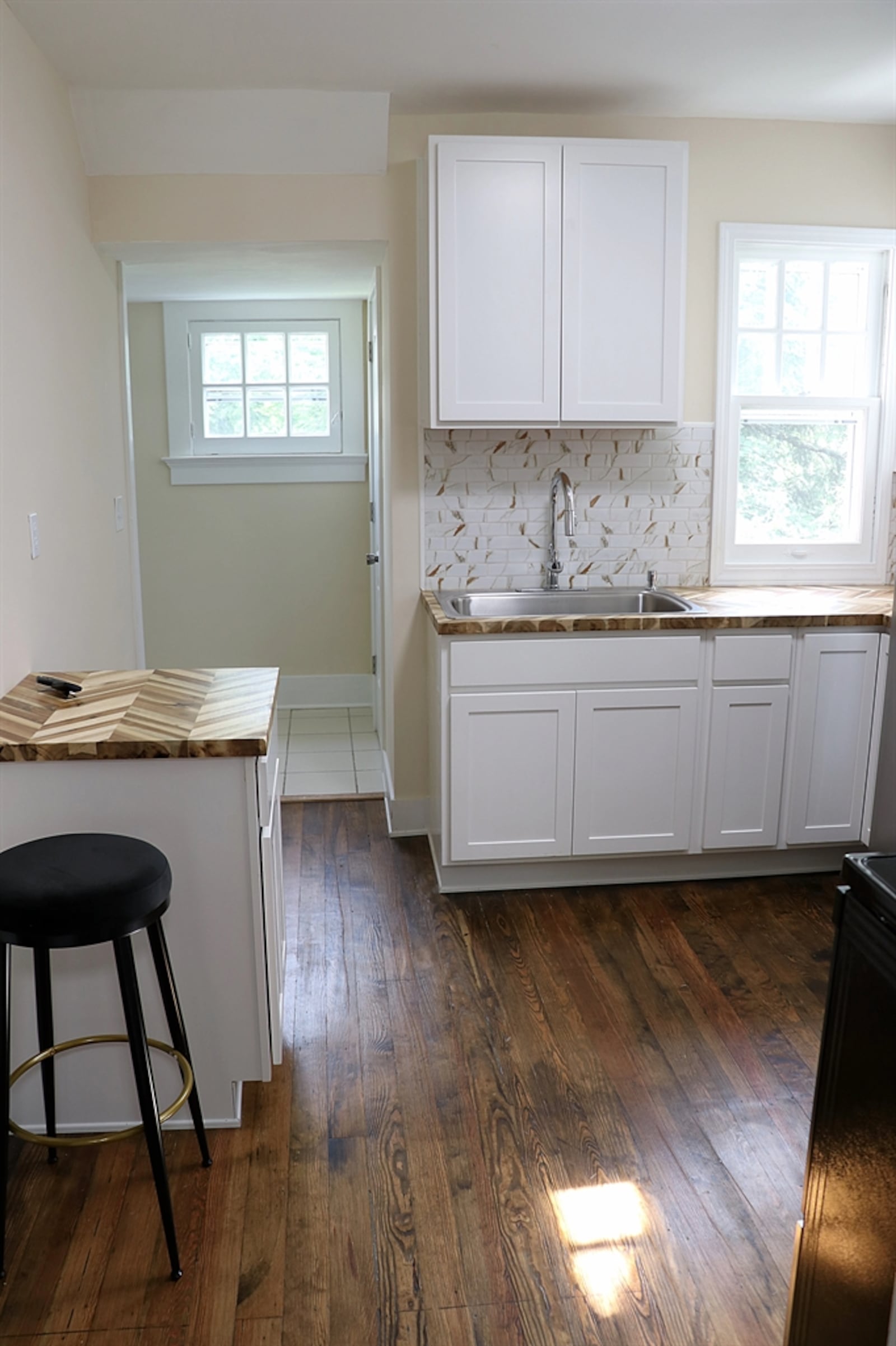 The kitchen has been redesigned with white cabinetry and chevron-plank wood counters. 