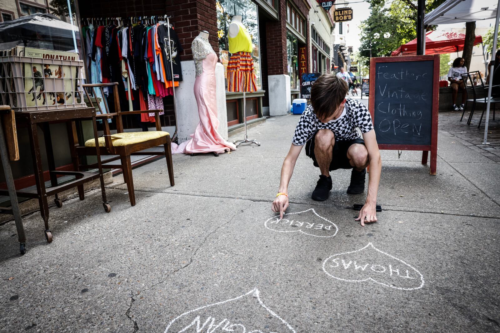 True Hoffman of Dayton's South Park neighborhood writes names on the sidewalk Friday, Aug. 4, 2023, of the nine victims of the Oregon District mass shooting ahead of a remembrance event to mark the four-year anniversary.  JIM NOELKER/STAFF