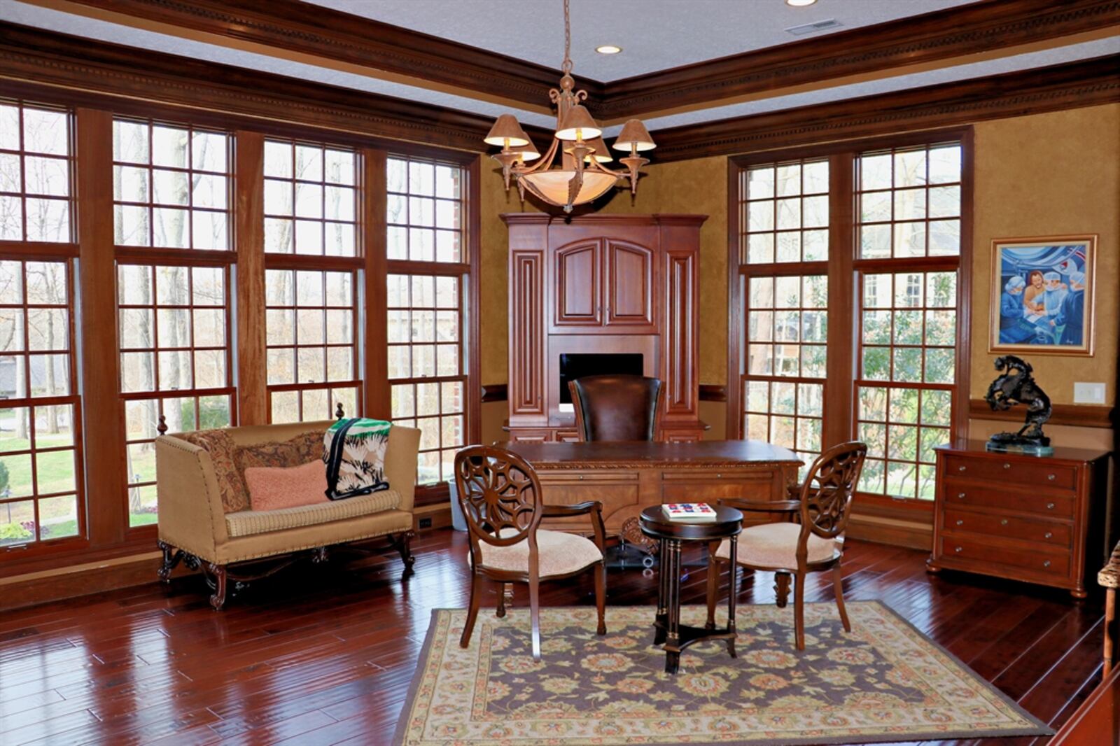 Floor-to ceiling windows fill the room with natural light and the tray ceiling has dentil crown molding. A glass door opens out to the side concrete driveway and boulder-steps to the backyard.