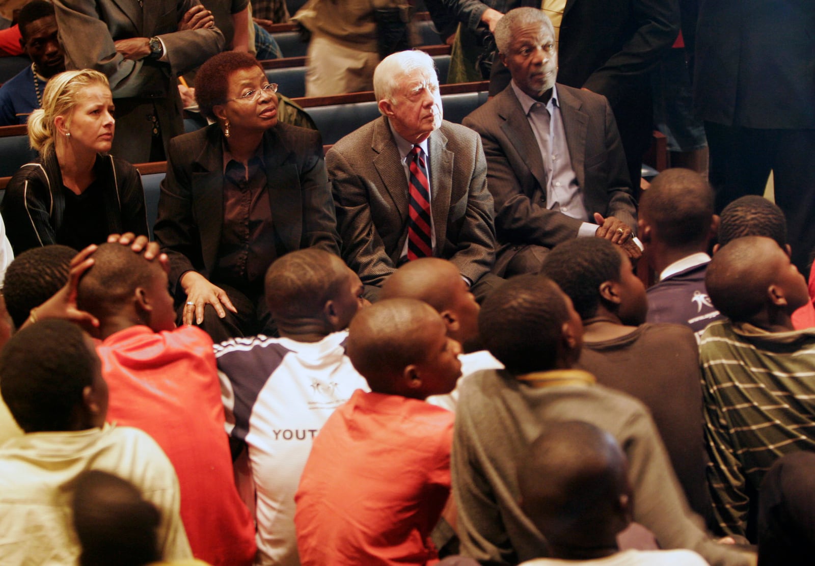 FILE - Former U.S. President Jimmy Carter, background second right, former U.N. head Kofi Annan, background right, and Graca Machel, the wife of former South African President Nelson Mandela, background second from left, watch children perform during a visit to the Central Methodist Church in Johannesburg, South Africa, Nov. 23, 2008. The diplomats were barred entry into Zimbabwe on a humanitarian visit over the weekend. (AP Photo/Denis Farrell, File)