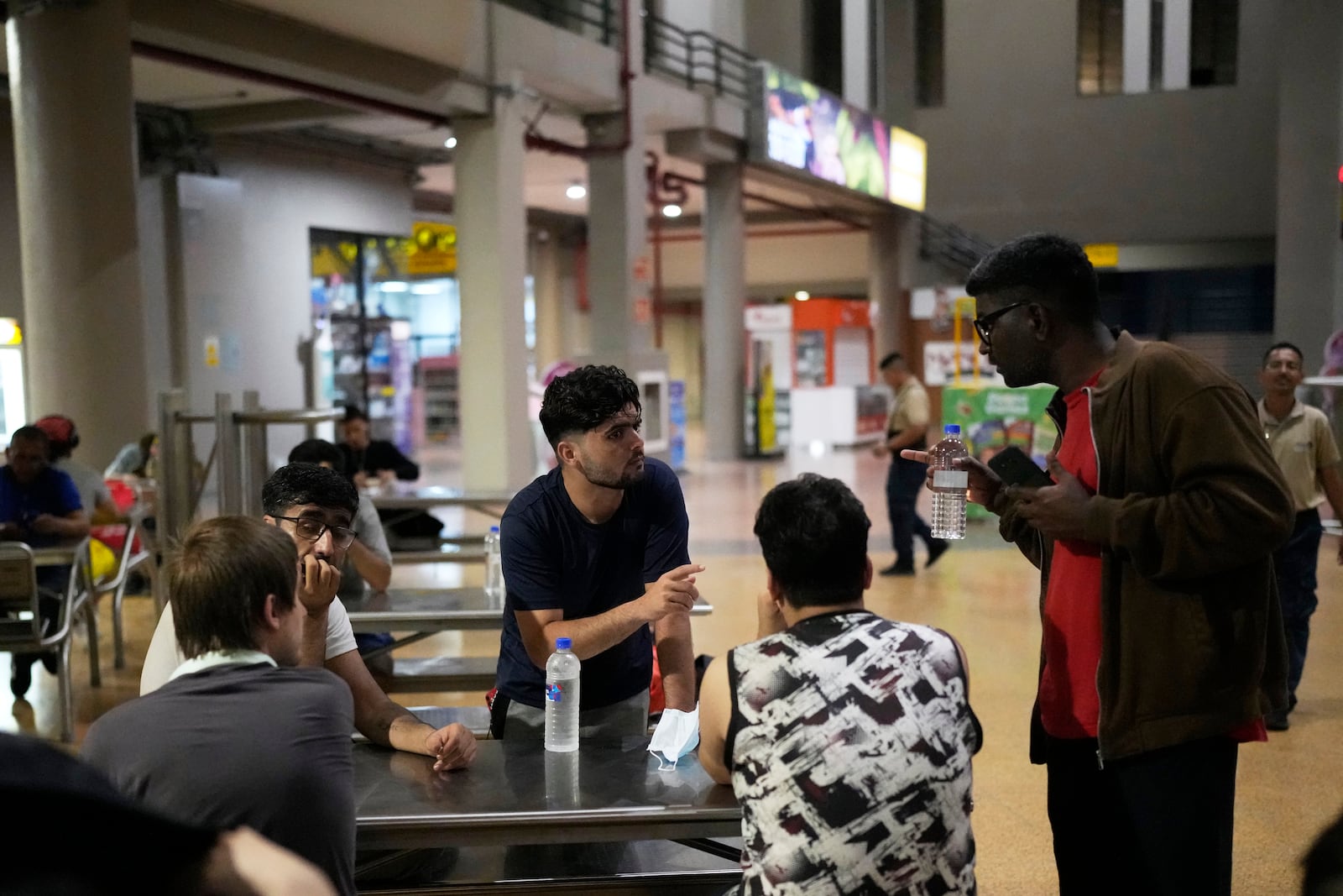 Samin Ihaider, of Pakistan, third from right, confers with other migrants at a shopping mall food court after arriving in Panama City on Saturday, March 8, 2025, following weeks in a Panamanian immigration camp after their deportation from the U.S. and release on the condition they leave the country within 30 days. (AP Photo/Matias Delacroix)