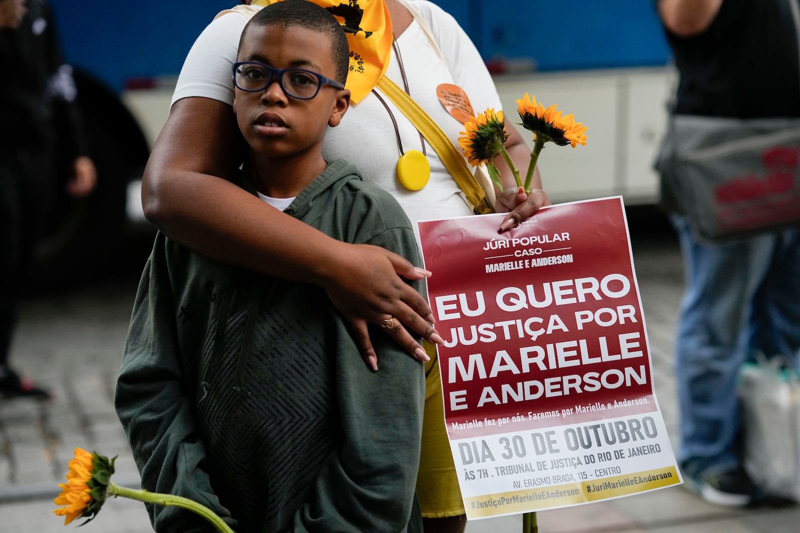 A demonstrator embraces a child while holding a sign with a message that reads in Portuguese: "I want justice for Marielle and Anderson", before the start of the trial of councilwoman Marielle Franco’s suspected murderers, outside the Court of Justice, in Rio de Janeiro, Brazil, Wednesday, Oct. 30, 2024. (AP Photo/Silvia Izquierdo)