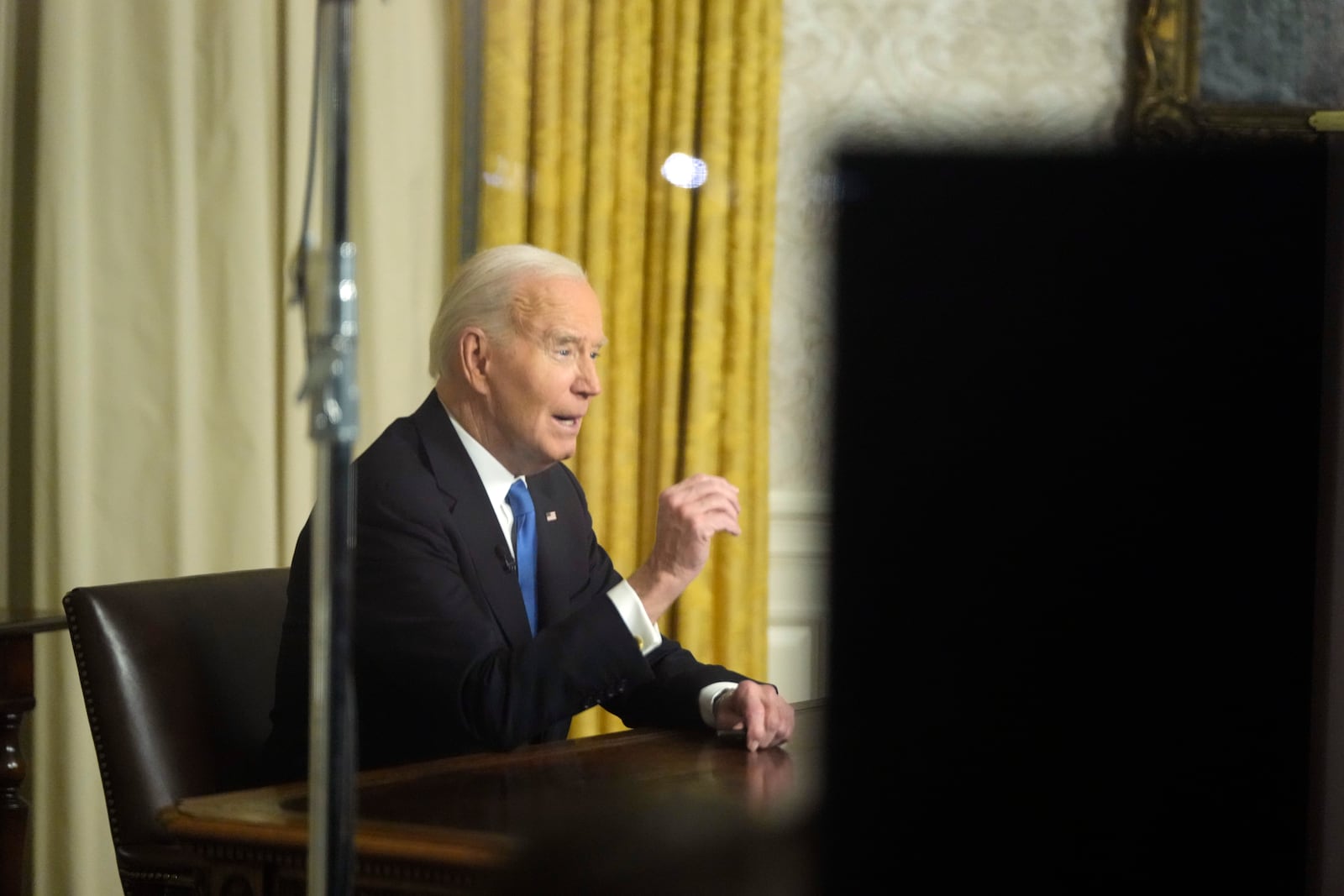 As seen through a window from the Colonnade outside the Oval Office, President Joe Biden speaks during his farewell address at the White House in Washington, Wednesday, Jan. 15, 2025. (AP Photo/Mark Schiefelbein)