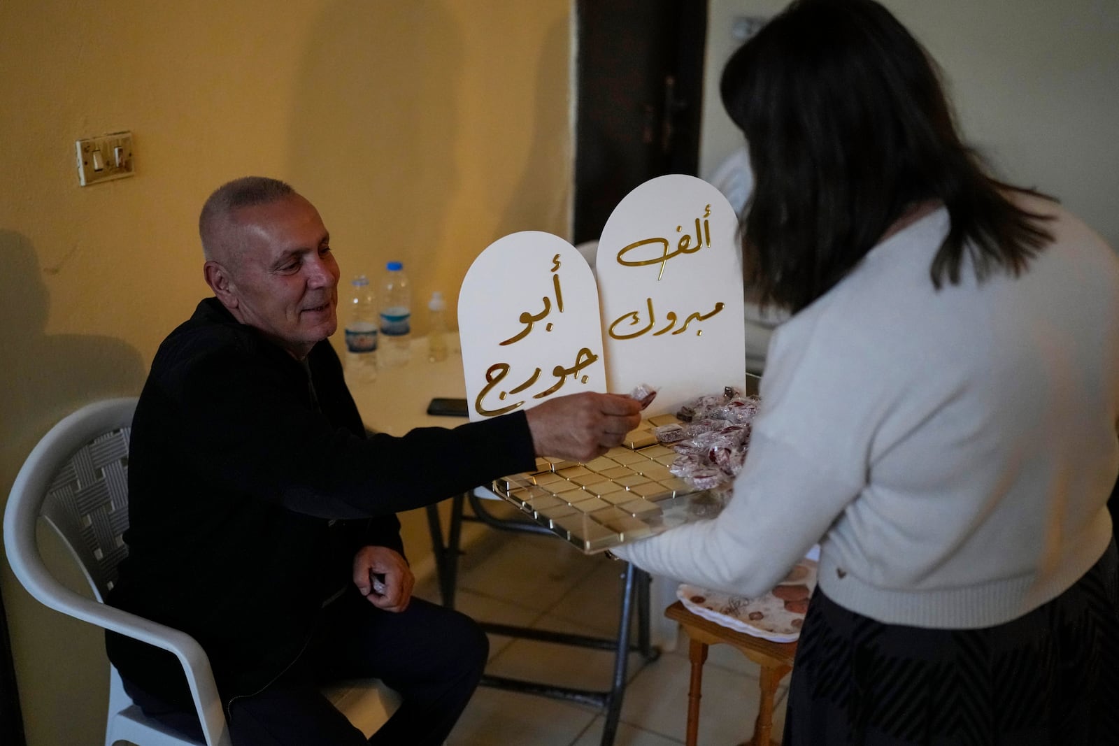 A woman distributes sweets to celebrate the return of Suheil Hamwi, who spent 32 years in prison in Syria and returned to Lebanon after the government of Bashar Assad was toppled, inside of his home in Chekka, Lebanon, Tuesday, Dec. 10, 2024. (AP Photo/Hassan Ammar)