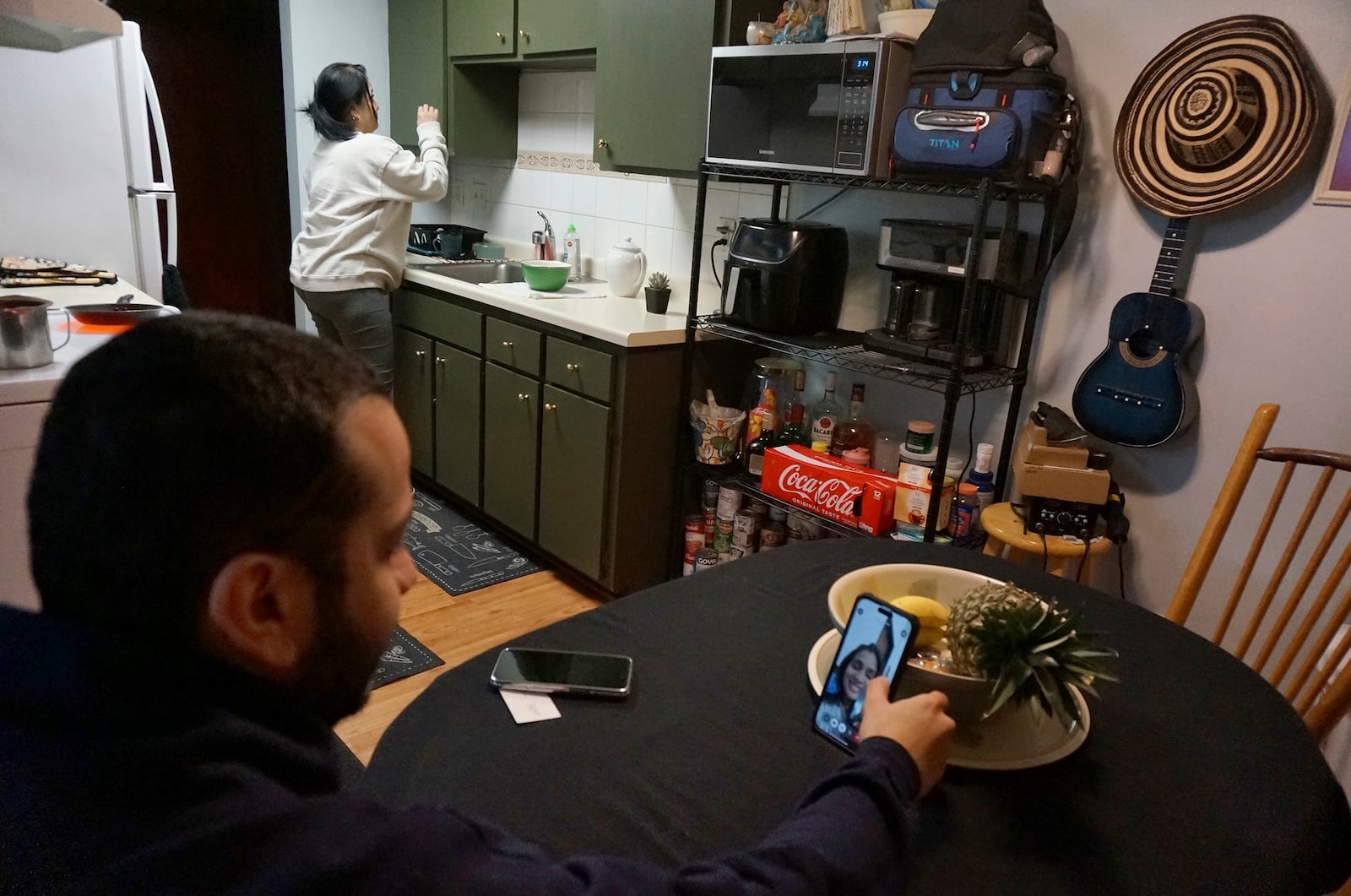 Johann Teran, a Venezuelan in the United States on humanitarian parole, talks in a video call with his wife, Karelia, who is stuck in Venezuela since her humanitarian program was canceled by the Trump administration, as her mother, Marlenia Padron, cooks at home in Hopkins, Minn., on Thursday, Feb. 13, 2025. (AP Photo/Giovanna Dell'Orto)