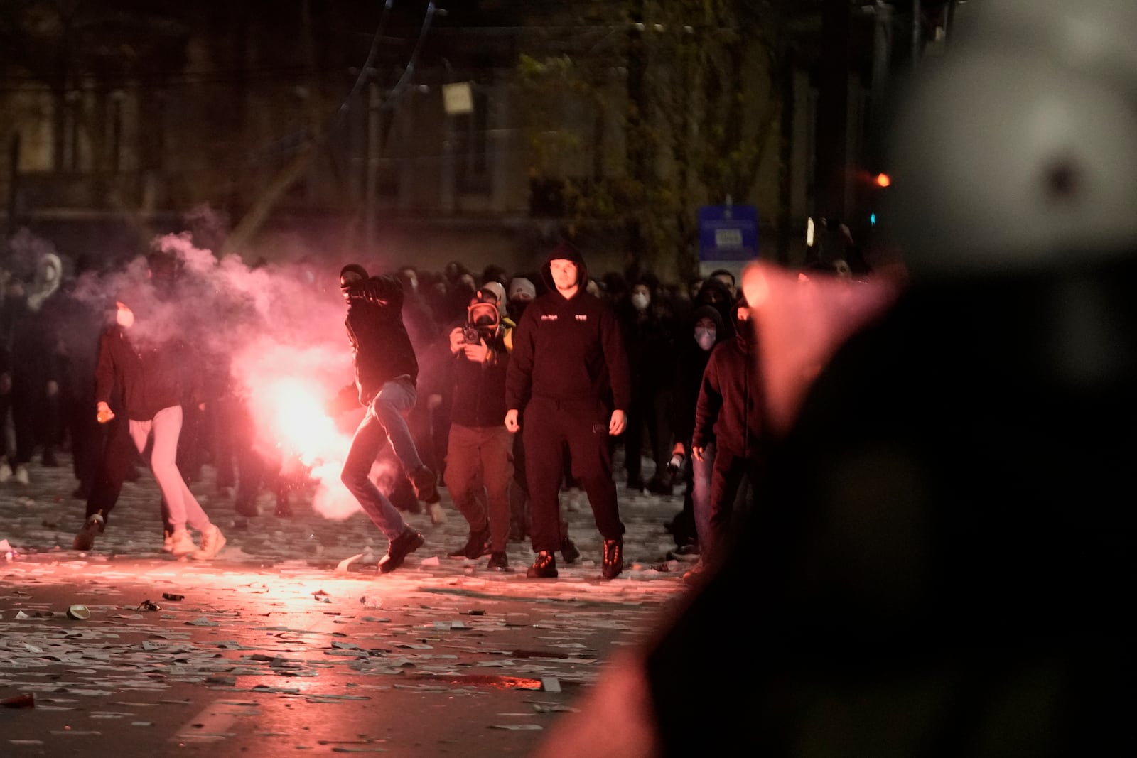 A hooded protester throws a smoke flare against riot police during clashes, after the Greek opposition parties have challenged the country's center-right government with a censure motion in parliament over a devastating rail disaster nearly two years ago, in Athens, Wednesday, March 5, 2025. (AP Photo/Petros Giannakouris)