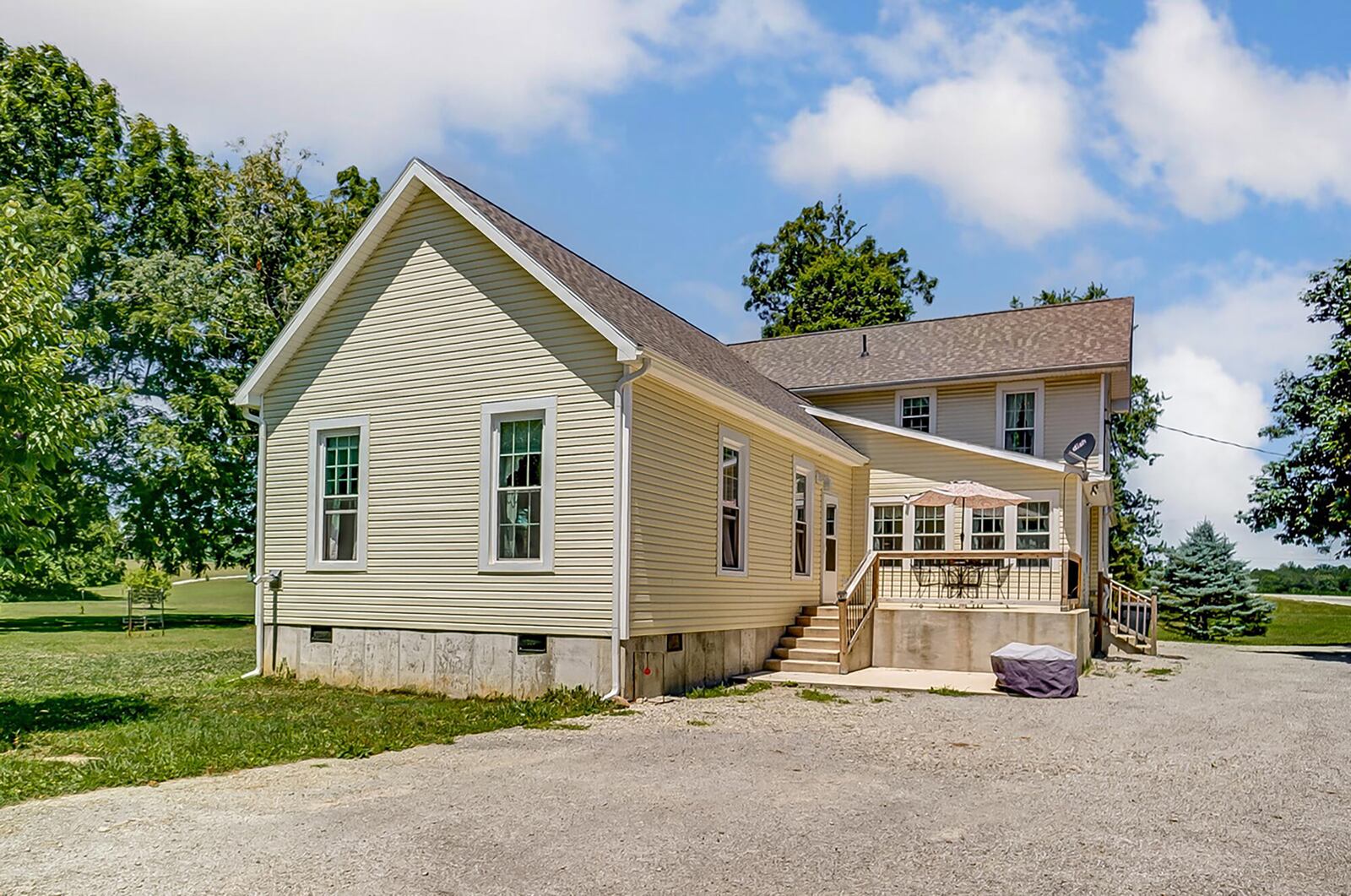 the rear of the home has a raised deck with railings leading to a concrete patio and long driveway connecting the road to the home and detached garage.