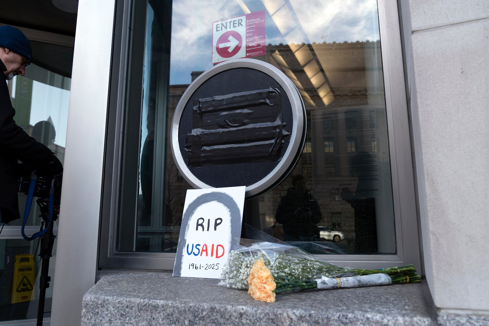 Flowers and a sign are placed outside the headquarters of the U.S. Agency for International Development, or USAID, Friday, Feb. 7, 2025, in Washington. (AP Photo/Jose Luis Magana)