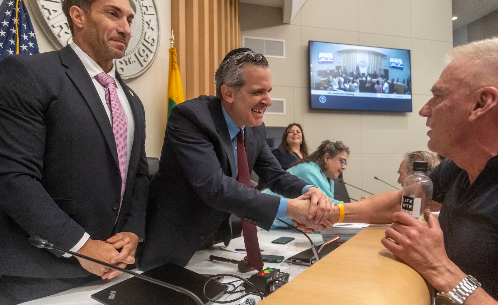 Miami Beach Mayor Steven Meiner, center, shakes hands with Miami Beach resident Edward Deveraux, right, after the Mayor withdrew resolution C7AA that would terminate O Cinema's lease and deferring resolution C7AB on Wednesday, March 19, 2025 in Miami Beach, Fla. (Jose Iglesias/Miami Herald via AP)