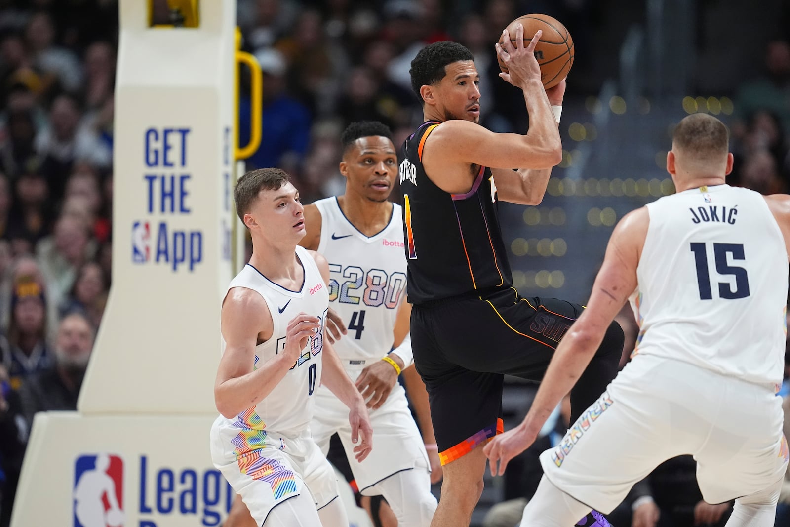 Phoenix Suns guard Devin Booker, third from left, passes the ball as, from left, Denver Nuggets guards Christian Braun and Russell Westbrook and center Nikola Jokic defend in the first half of an NBA basketball game Friday, March 7, 2025, in Denver. (AP Photo/David Zalubowski)