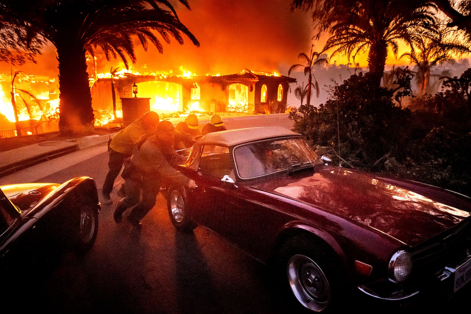 Firefighters and sheriff's deputies push a vintage MG away from a burning home as the Mountain Fire burns in Camarillo, Calif., on Wednesday, Nov. 6, 2024. (AP Photo/Noah Berger)