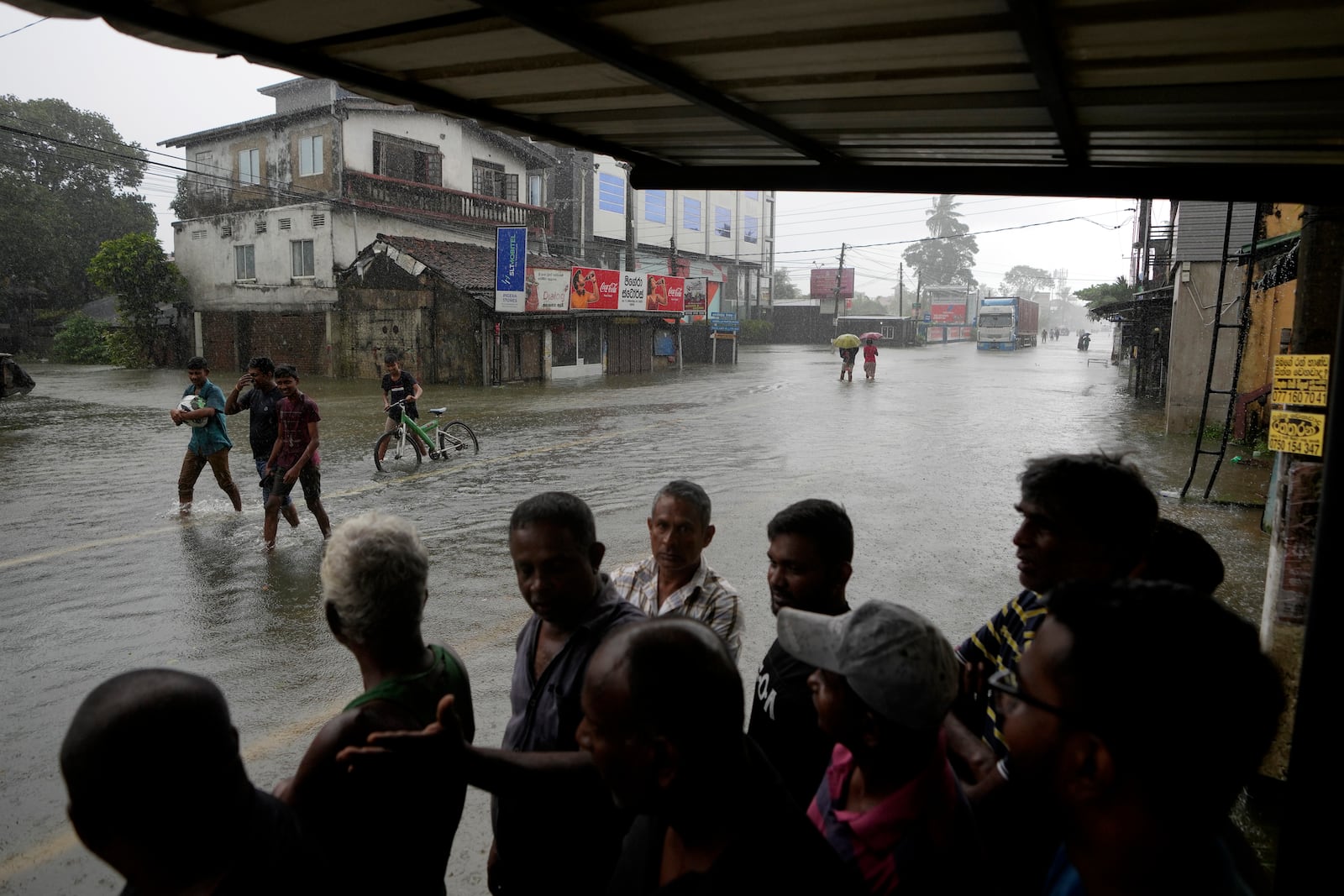 People takes shelter as it rains while others wade through a flooded street in Colombo, Sri Lanka, Sunday, Oct. 13, 2024. (AP Photo/Eranga Jayawardena)