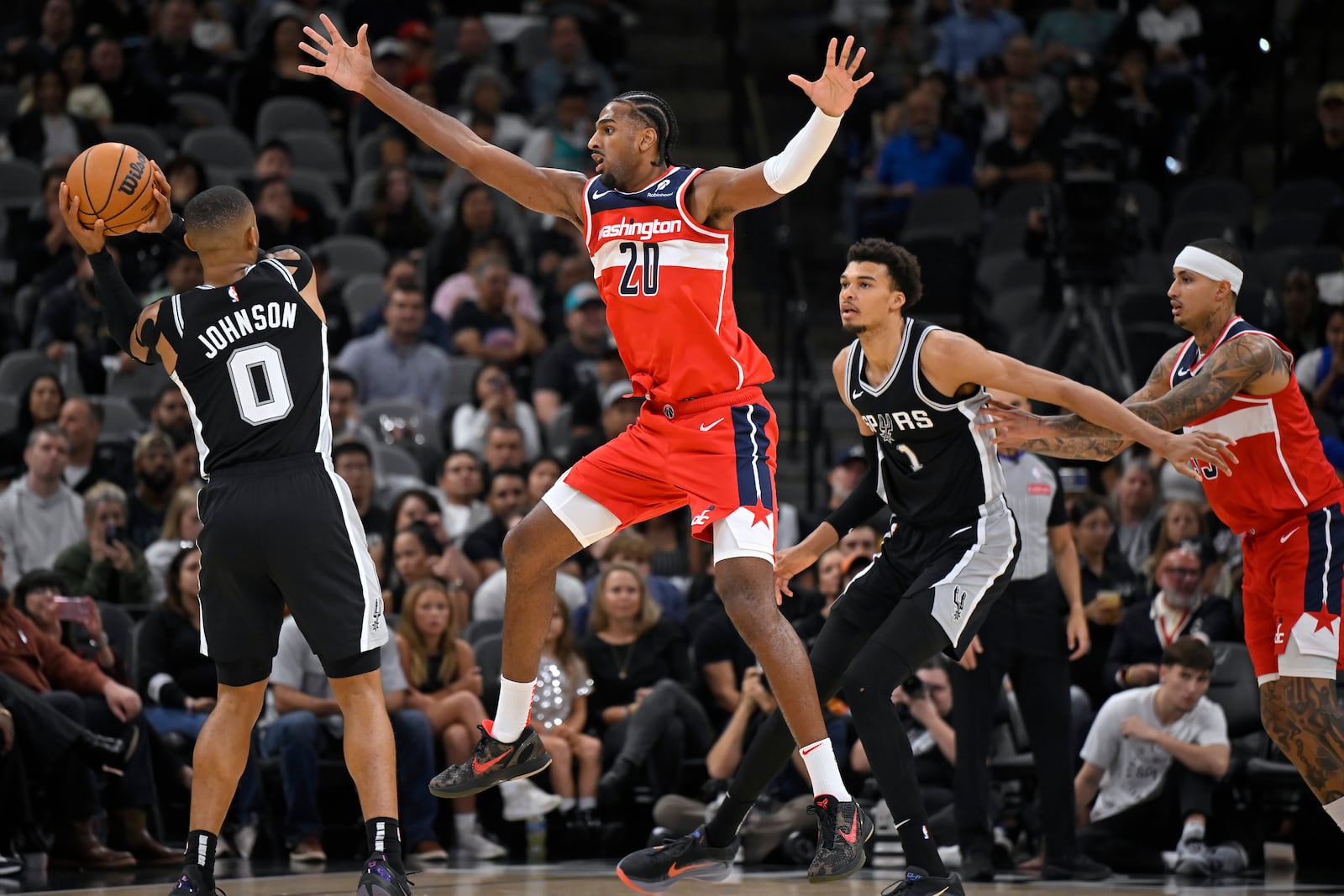 San Antonio Spurs' Keldon Johnson (0) looks to pass as he is defended by Washington Wizards' Alex Sarr (20) during the first half of an NBA basketball game, Thursday, Nov. 13, 2024, in San Antonio. (AP Photo/Darren Abate)