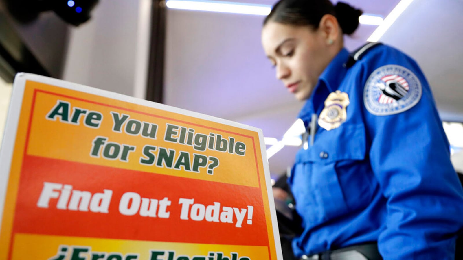 A Transportation Security Administration employee stands at a booth to learn about a food stamp program at a food drive at Newark Liberty International Airport, Wednesday, Jan. 23, 2019, in Newark, N.J. TSA employees each received a box of non perishables and a bag of produce to help them during the shutdown.