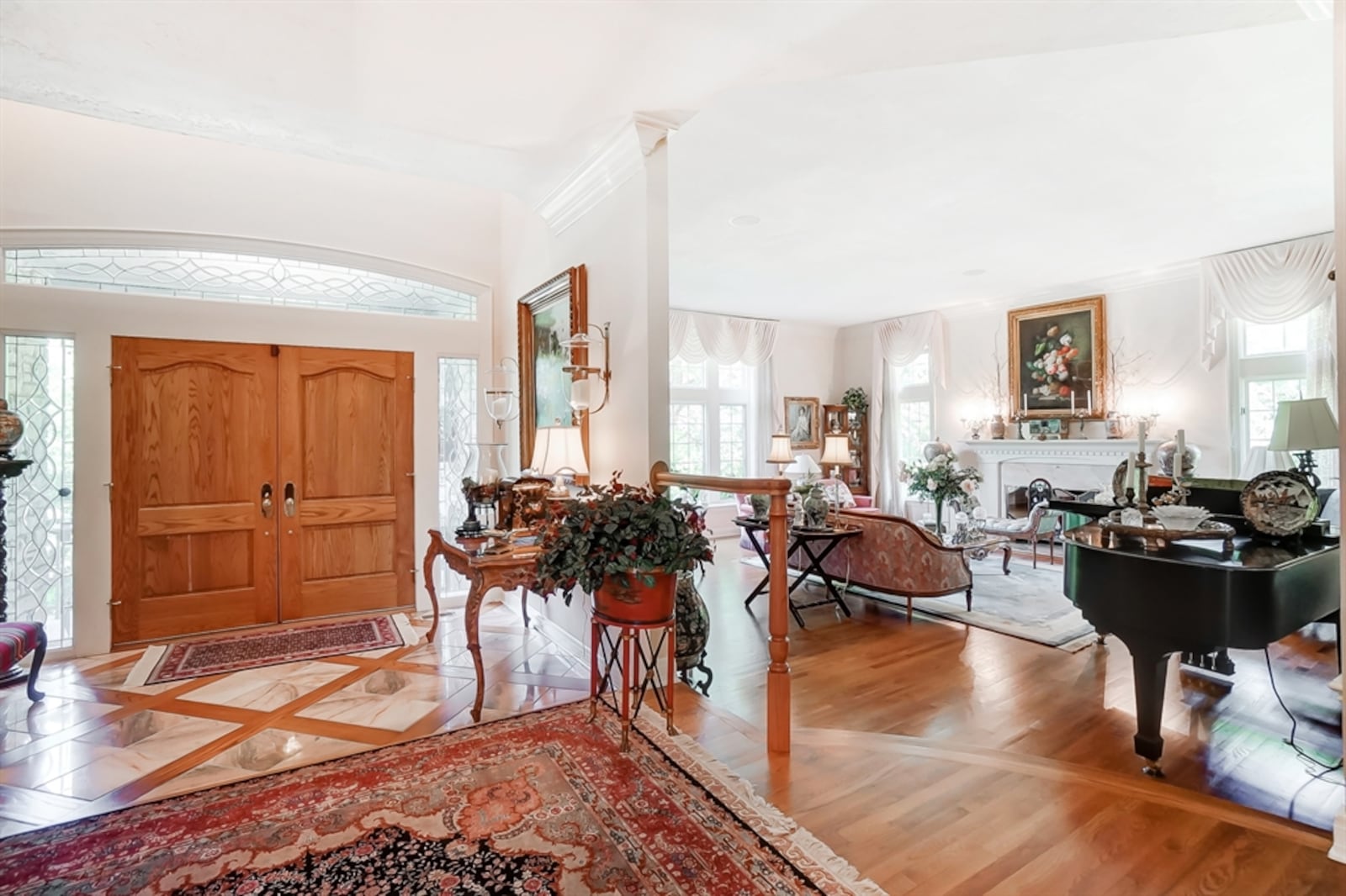 Double doors surrounded by leaded-glass sidelights and a transom open into the foyer with wood-framed marble flooring. 