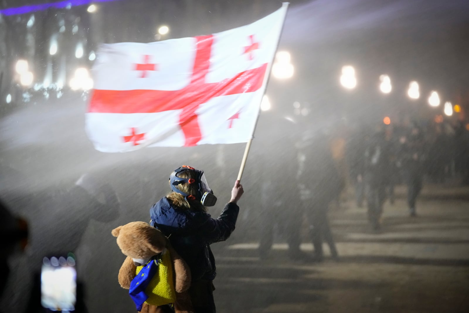 A demonstrator holds a Georgian national flag while being sprayed by a water cannon outside the parliament during a protest against the government's decision to suspend negotiations on joining the European Union in Tbilisi, Georgia, on Tuesday, Dec. 3, 2024. (AP Photo/Pavel Bednyakov)