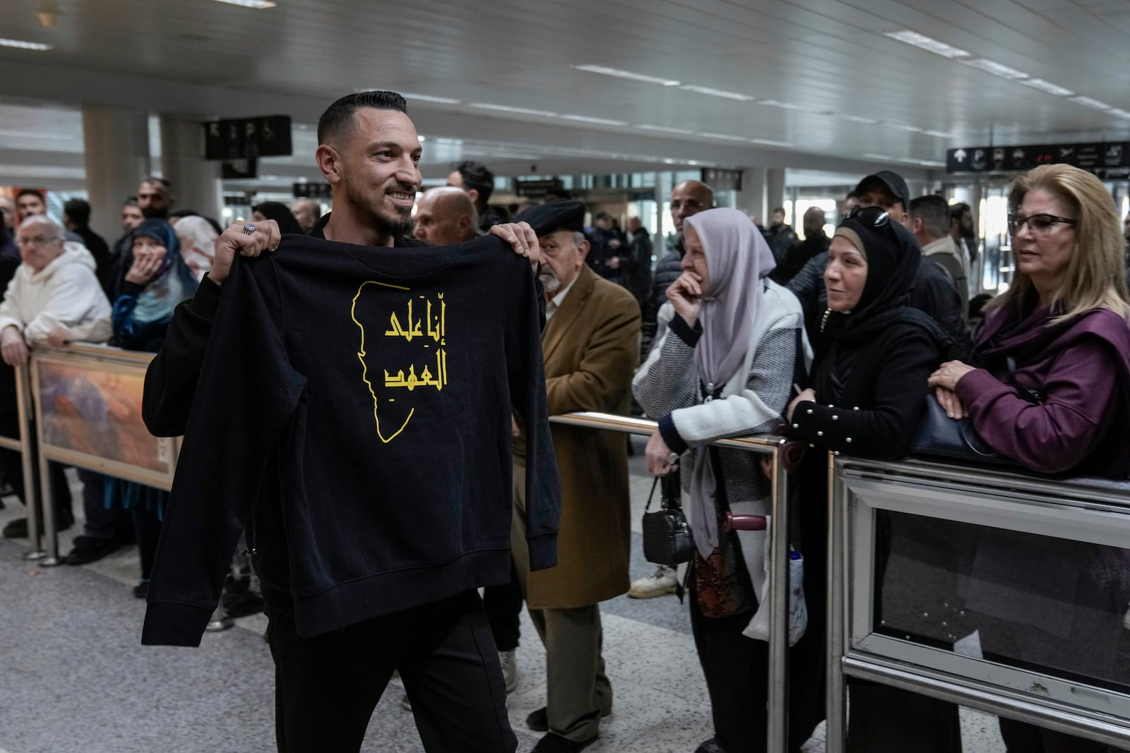 A Hezbollah supporter displays a t-shirt with Arabic words that read "We are committed to the covenant" as he arrives at the Rafik Hariri International Airport, in Beirut, Lebanon, Friday, Feb. 21, 2025. (AP Photo/Bilal Hussein)