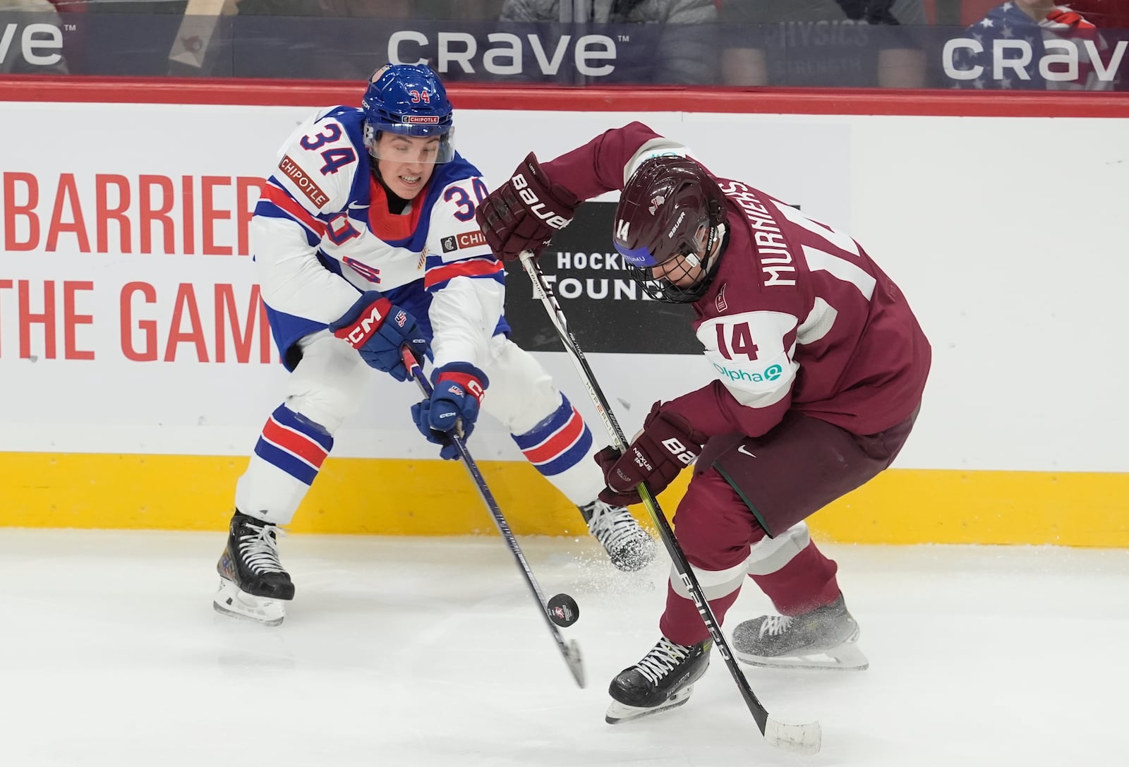 United States forward Gabe Perreault (34) pokes the puck away from Latvia forward Olivers Murnieks (14) during the first period of a IIHF World Junior Hockey Championship tournament game, Saturday, Dec.28, 2024 in Ottawa, Ontario. (Adrian Wyld/The Canadian Press via AP)