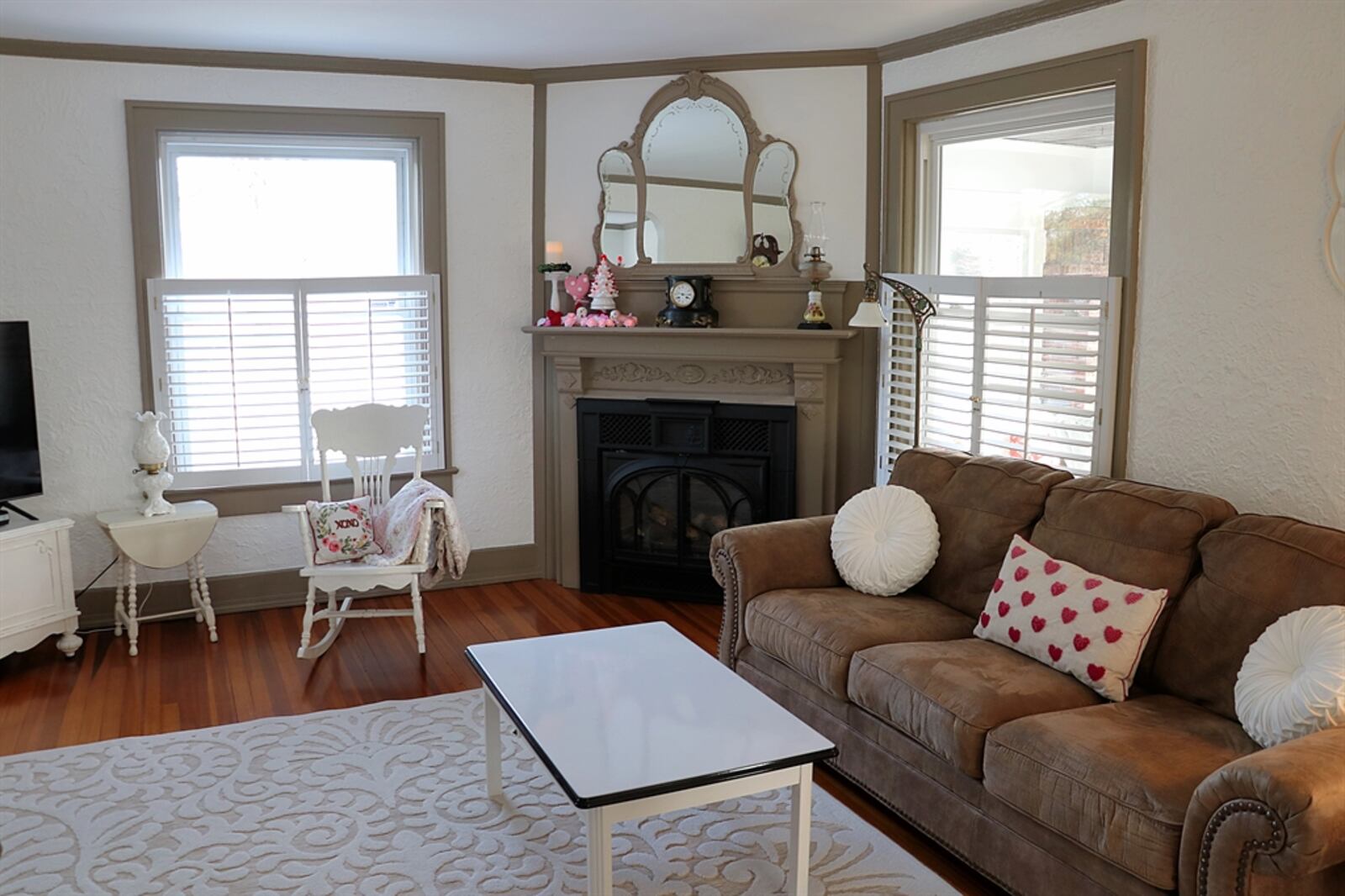 Tucked into one corner of the living room is a gas fireplace with painted wood ornate mantel. The wood accents surround a kidney-shaped triple mirror. The fireplace is angled within the corner so that it can be enjoyed from the entire living room and the adjoining dining room.